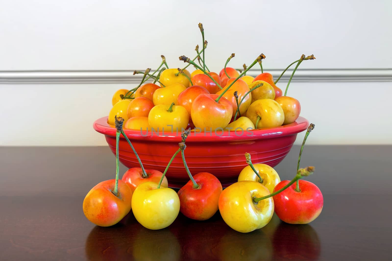 Pile of Rainier Cherries in a red bowl and on a wooden table closeup