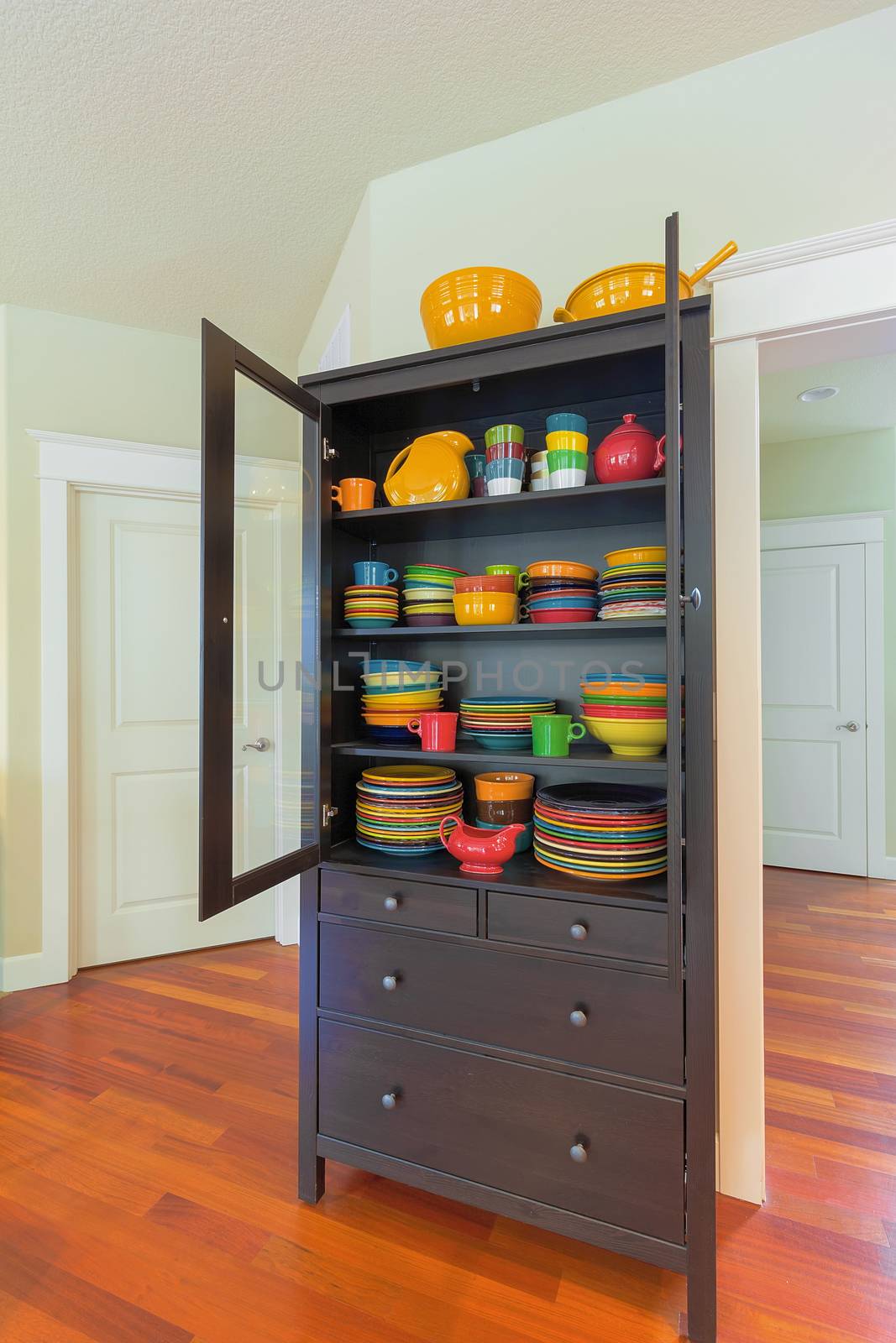 Cupboard with colorful stoneware dinnerware in home with cherry hardwood floor