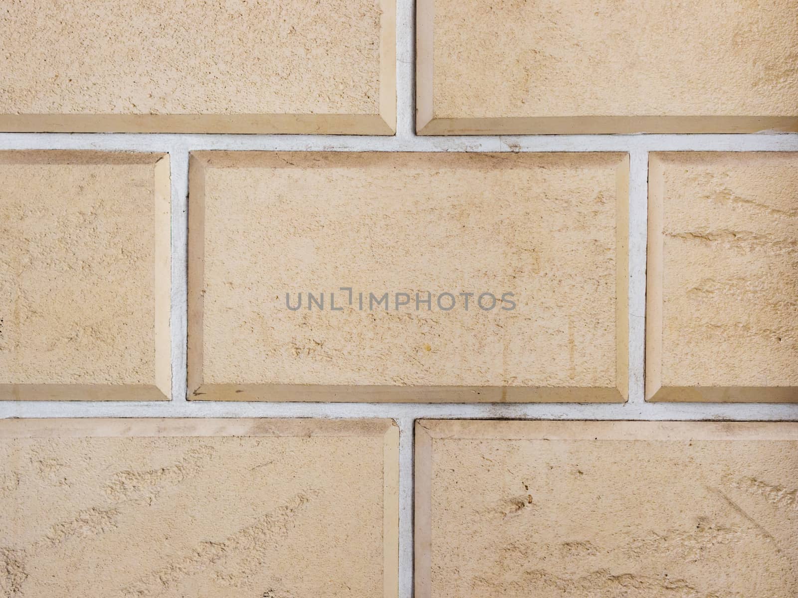 a wall from an artificial beige stone facade with rough fractured surfaces, laid as a brick