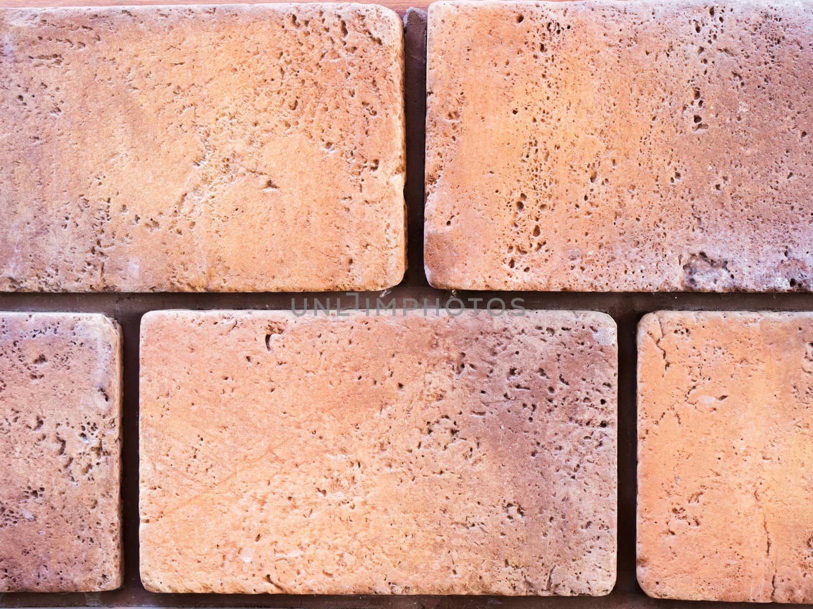 a wall from an artificial beige and red stone facade with rough fractured surfaces, laid as a brick