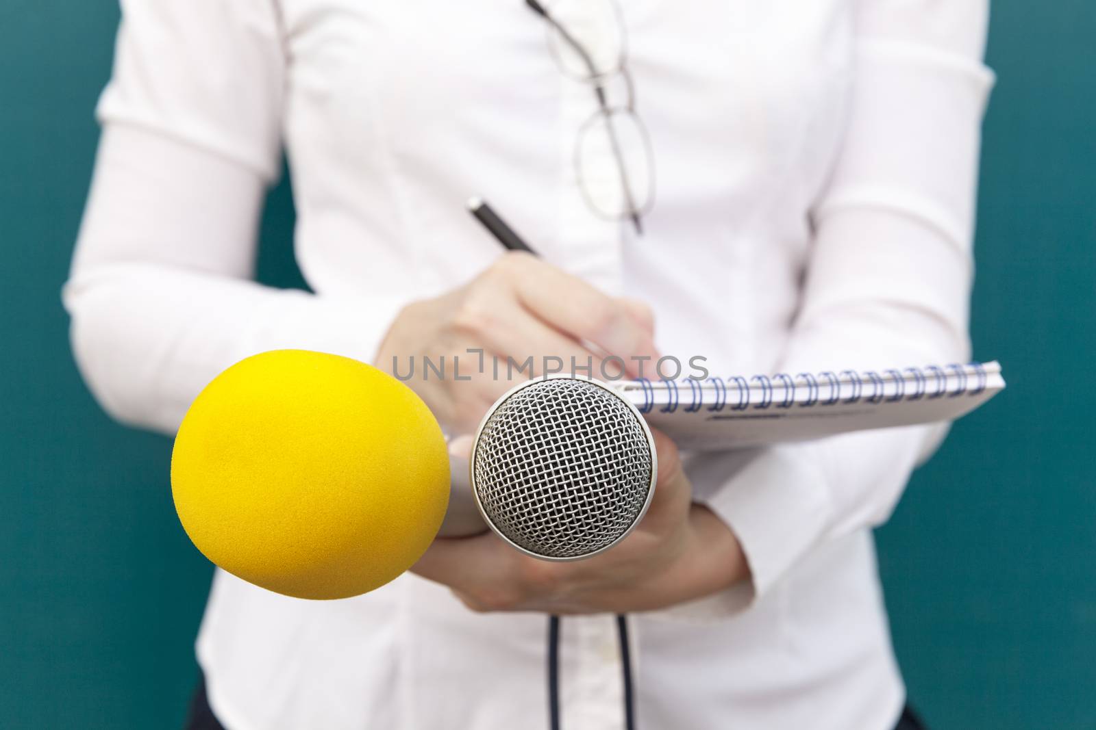 Female reporter or journalist at news conference, writing notes, holding microphones