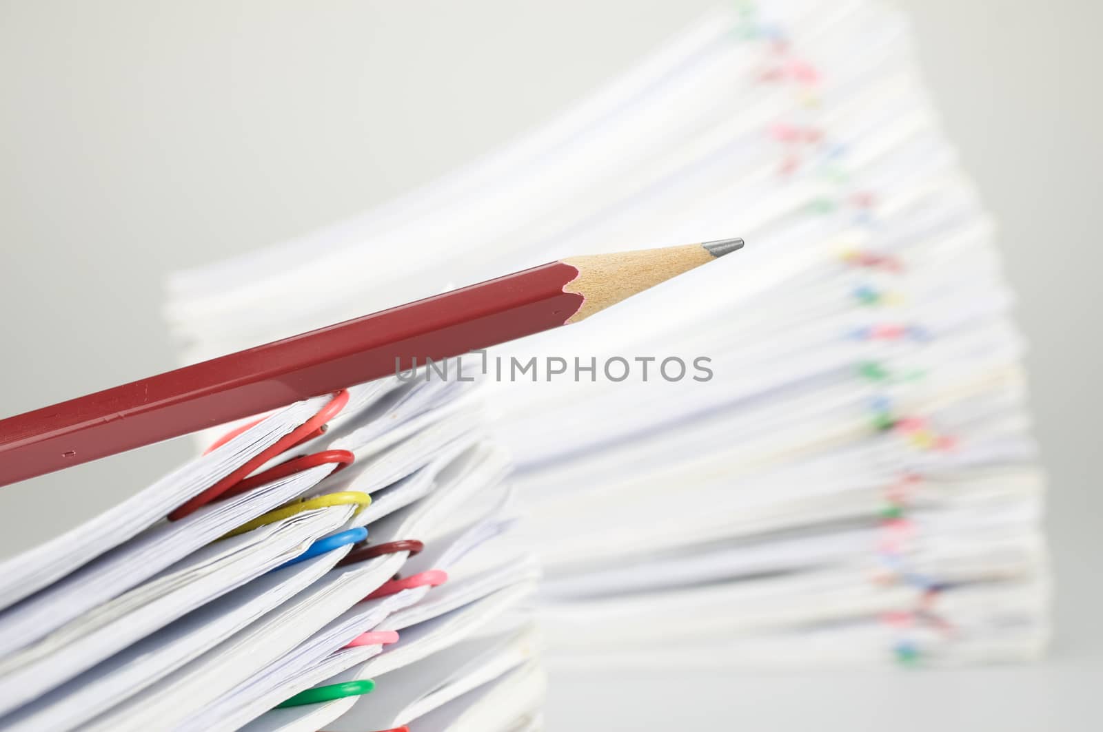 Close up pencil on document have blur pile overload paperwork of report and receipt with colorful paperclip place on white background.