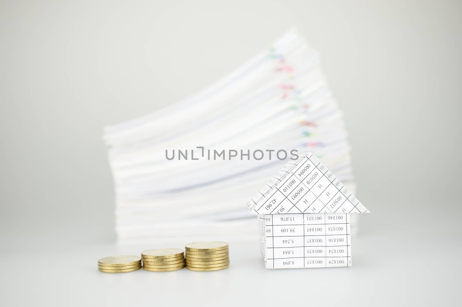 Close up step of gold coins and house have blur pile overload paperwork of report and receipt with colorful paperclip place on white background.