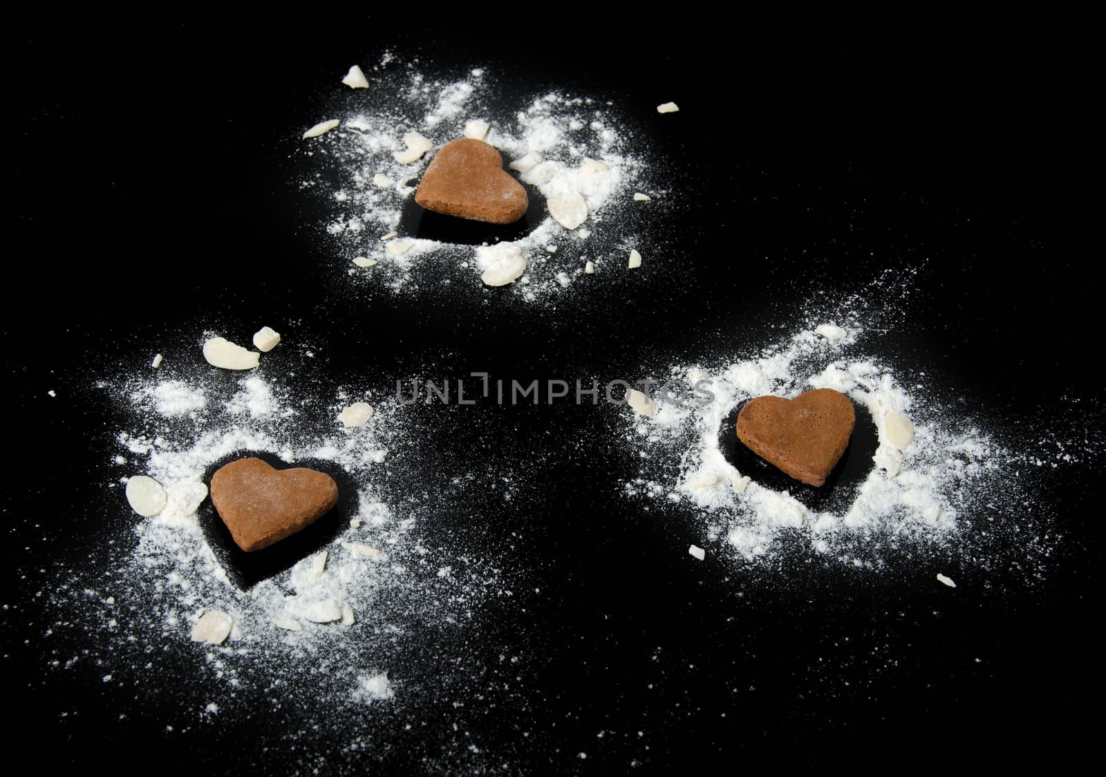 Three gingerbread hearts with almond and flour isolated on black background.
