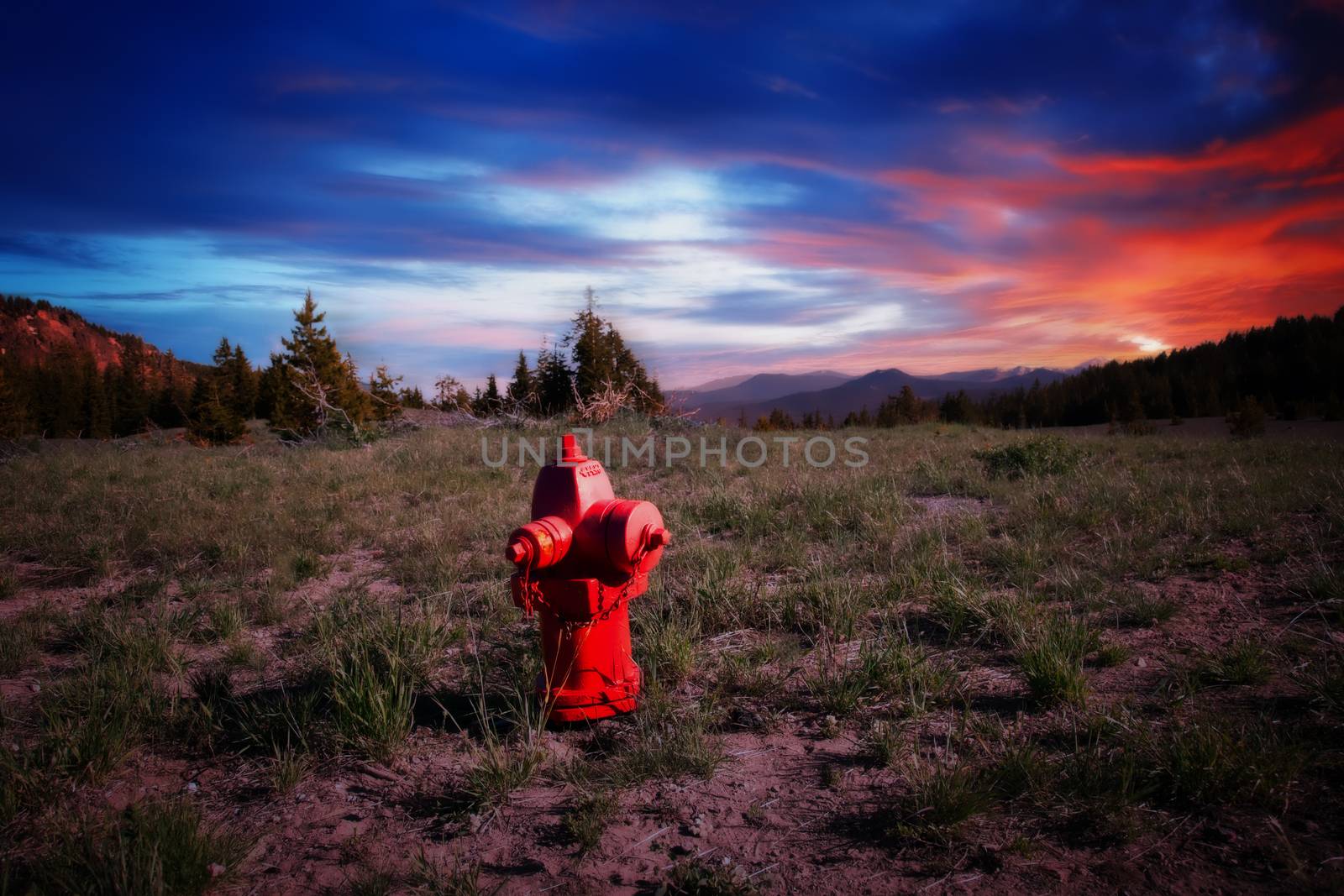 A red fire hydrant in the middle of a field with a colorful sunset in the background.