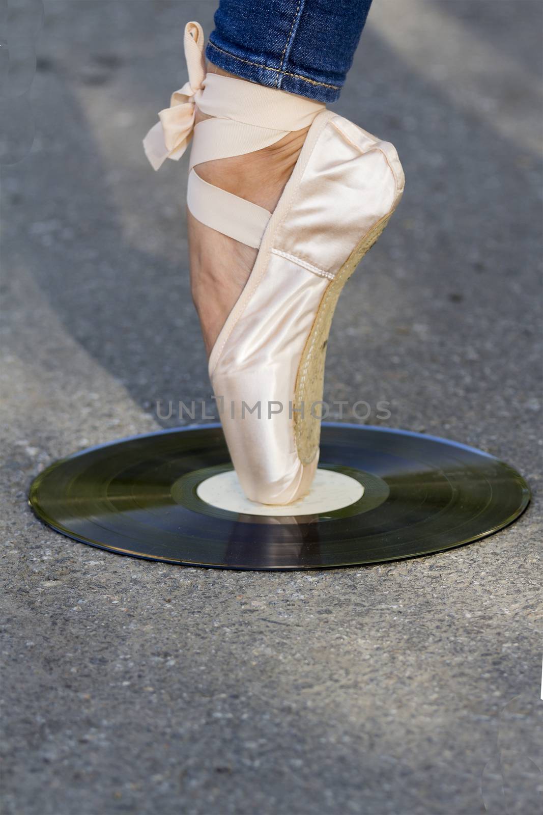 Foot girls in Ballet shoes  stands on a vinyl disc, which lies on the road.