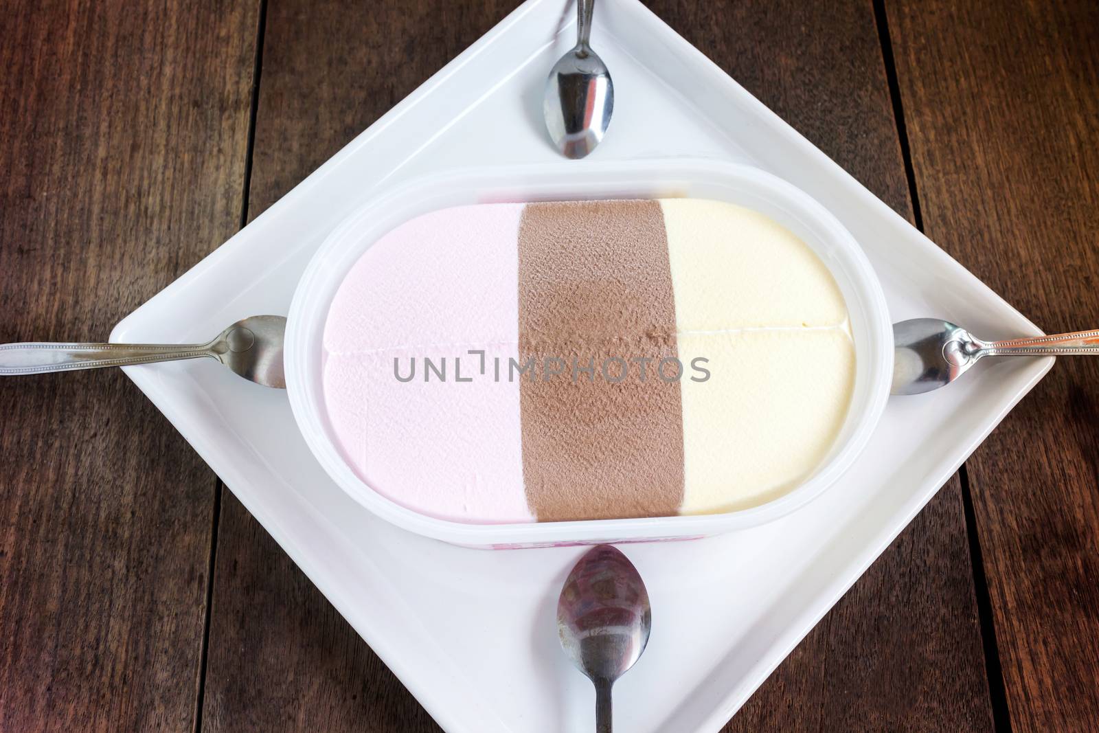 Top view icecream vanilla,strawberry and chocolate flavour on white plate with spoons on wood table