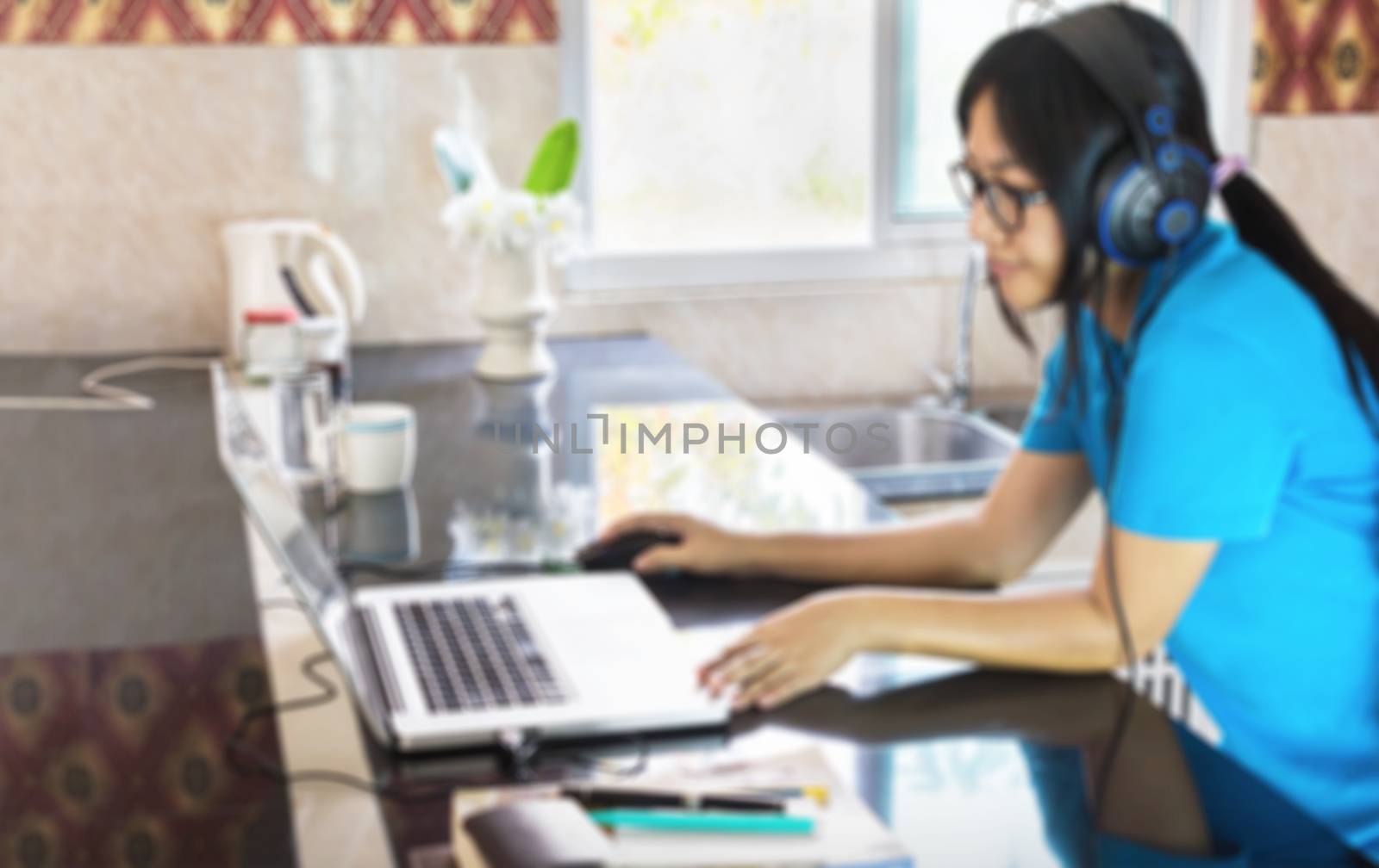 Blurred picture of relaxing life style Asian girl serfing internet or data search on notebook at counter in home 