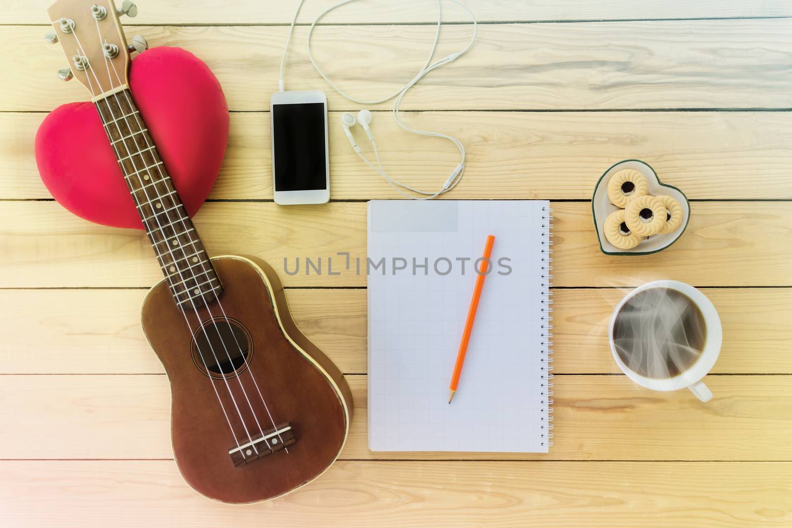 Blank note book and pencil with coffee,cookie, mobile phone and ukulele in vintage style on jointed wooden background