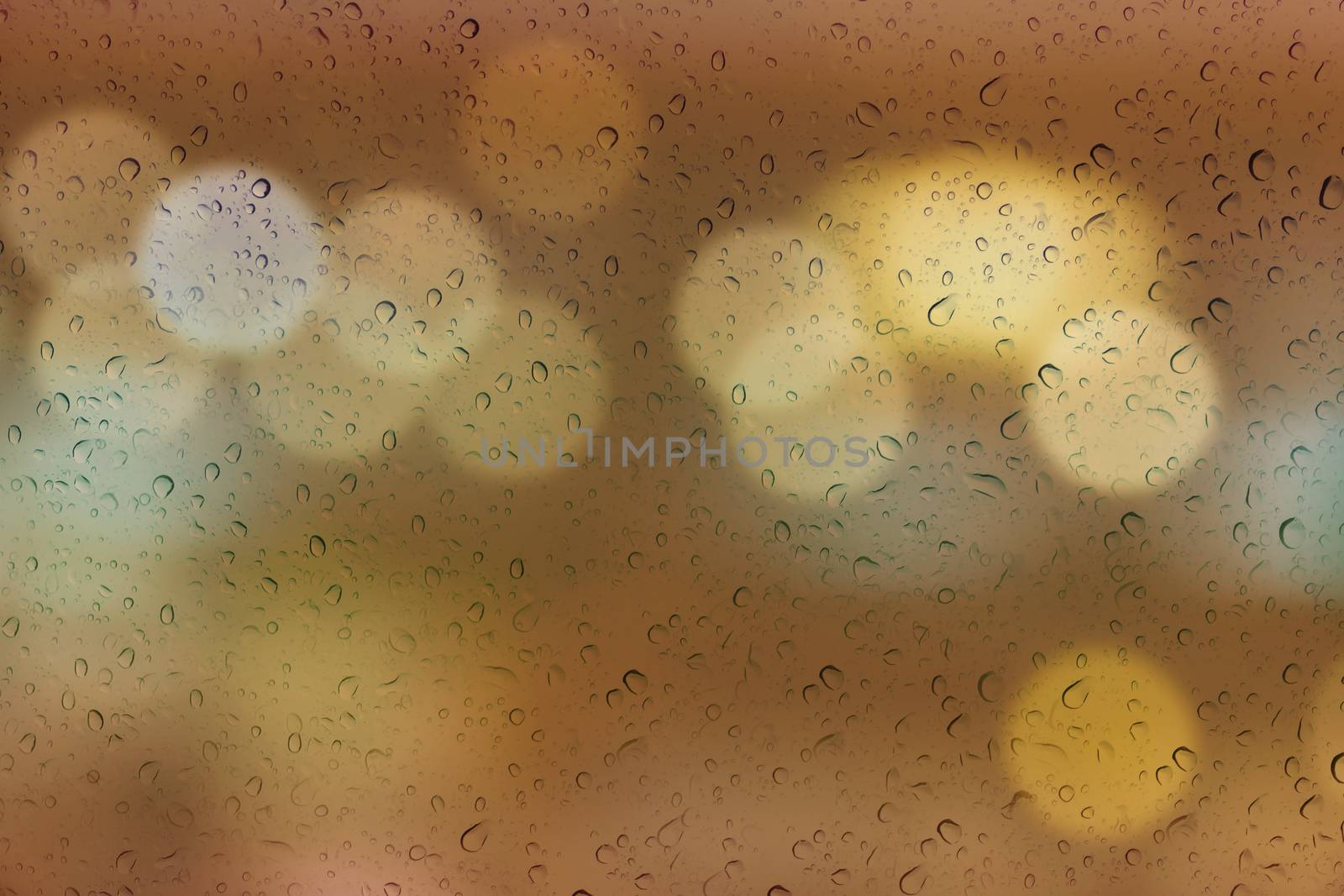 Water or rain drop on mirror glass plate window with bokeh abstract soft orange gold background