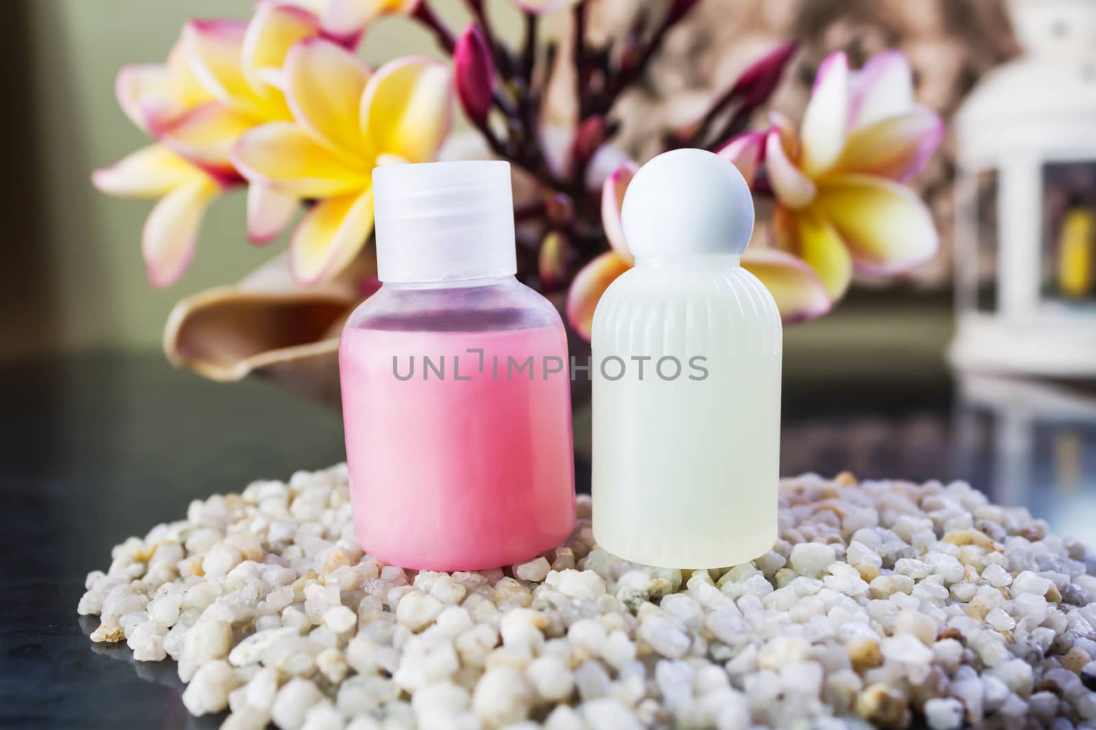Mini set of shower bath soap, shampoo,conditioner on pebble and flower background