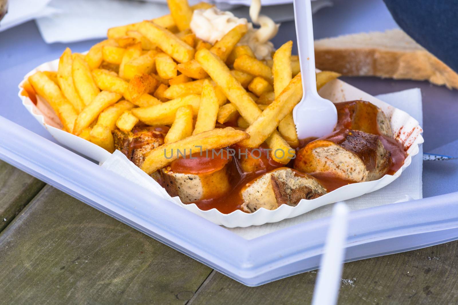 A paper tray with currywurst and French fries  on an old wooden table.