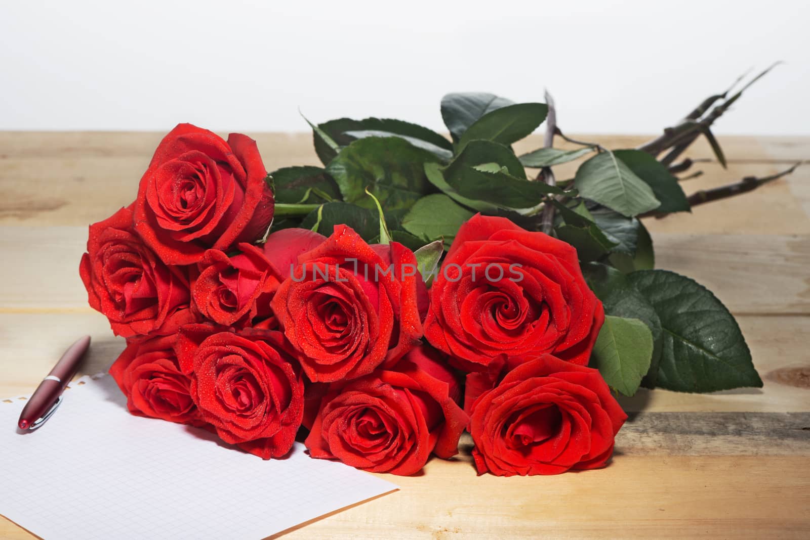 Bouquet of scarlet roses on a surface from wooden boards and the sheet of white paper for writing of the text