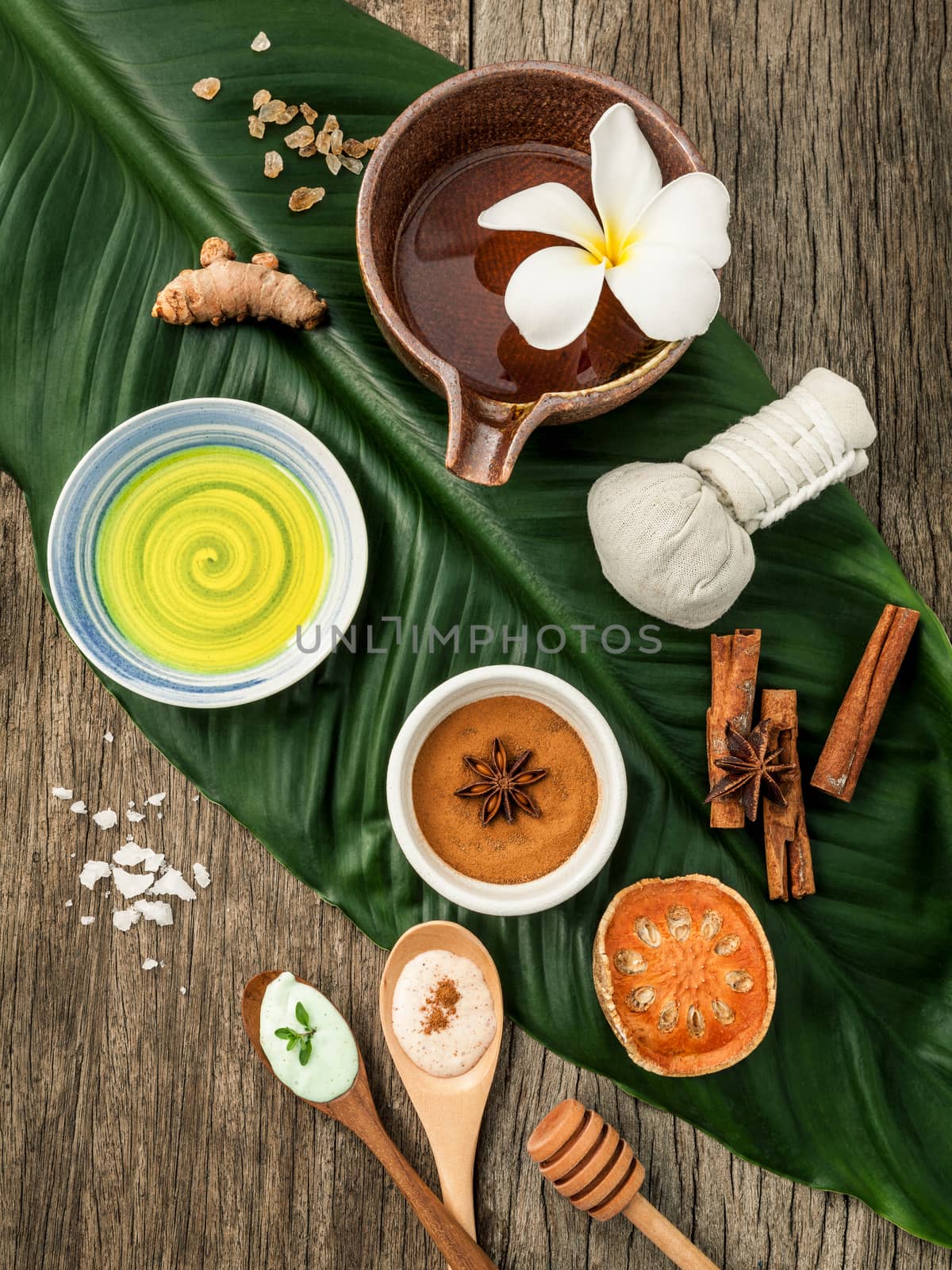 Green leaves with nature spa ingredients turmeric,herbal compress ball,dried indian bael ,cinnamon powder ,cinnamon sticks ,aromatic oil ,star anise and sea salt on rustic background.
