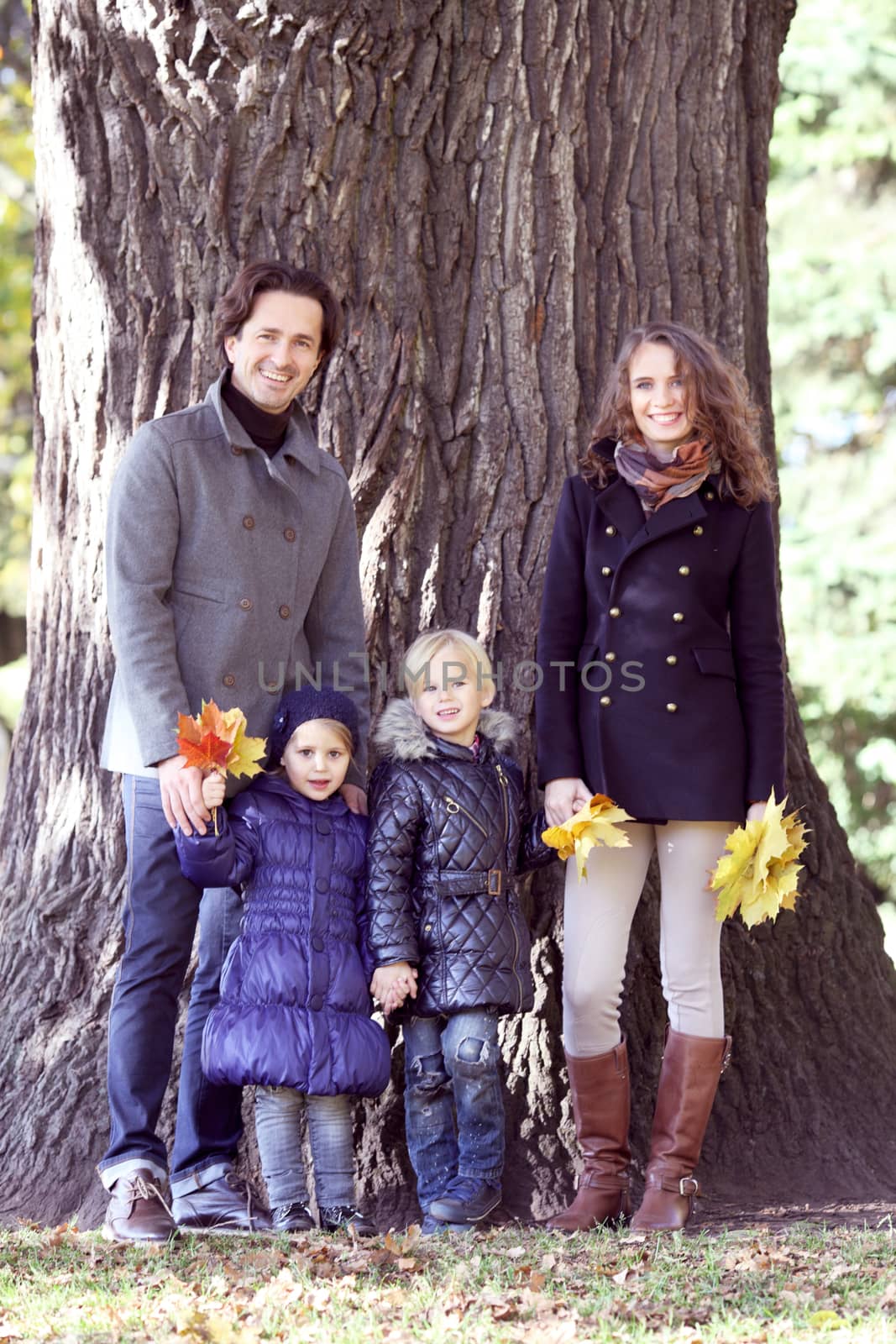 Happy family in autumn park near big tree trunk