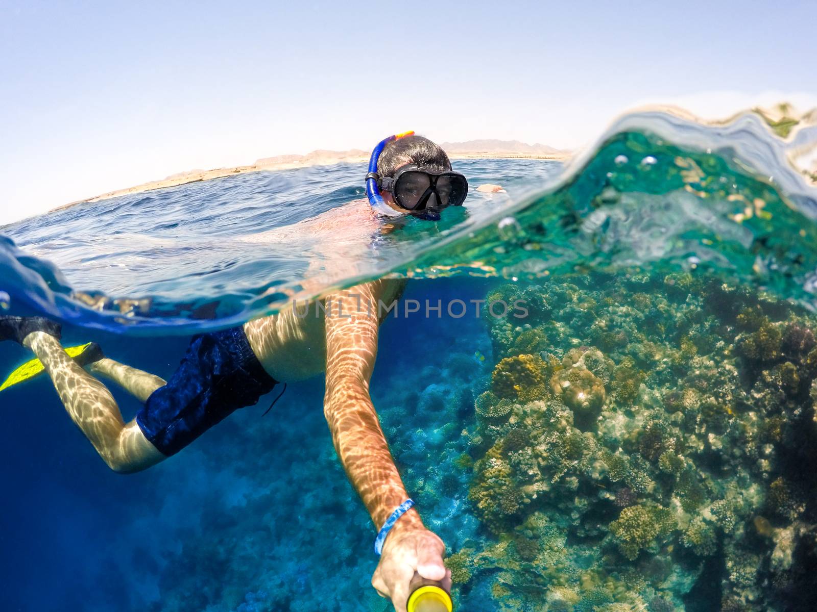 Underwater and surface split view in the tropics paradise with snorkeling man, fish and coral reef, under and above waterline, beautiful view on tropical sea. Safaga, Egypt. Holiday snorkeling vacation concept