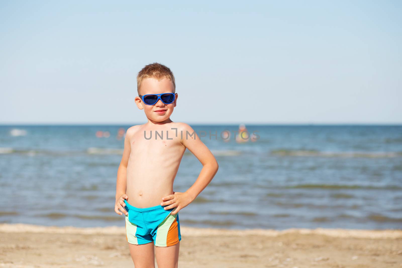 Little kid wearing fashion sunglasses on the beach on hot summer day. Smiling boy playing on the beach. Child is going to swim in the sea. Summer vacation