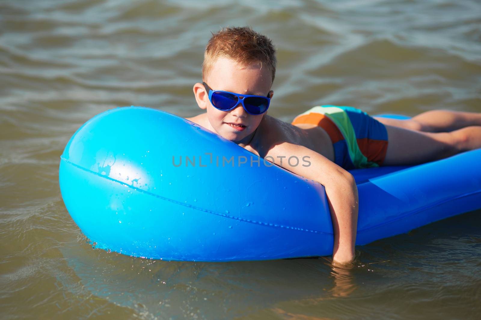 Little kid swimming in the sea on inflatable mattress. Smiling boy playing on the beach with air mattress. Summer vacation