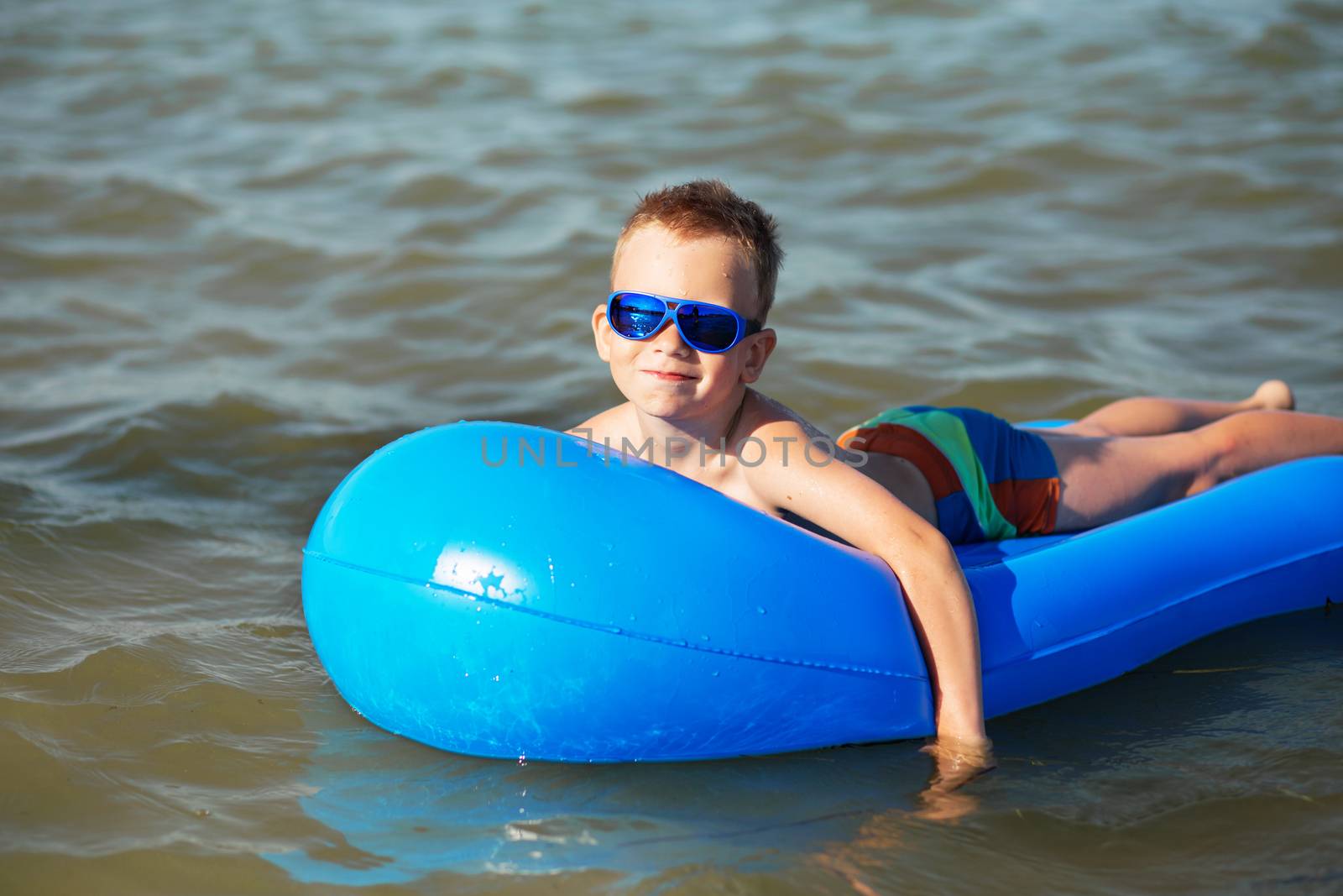 Little kid swimming in the sea on inflatable mattress. Smiling boy playing on the beach with air mattress. Summer vacation