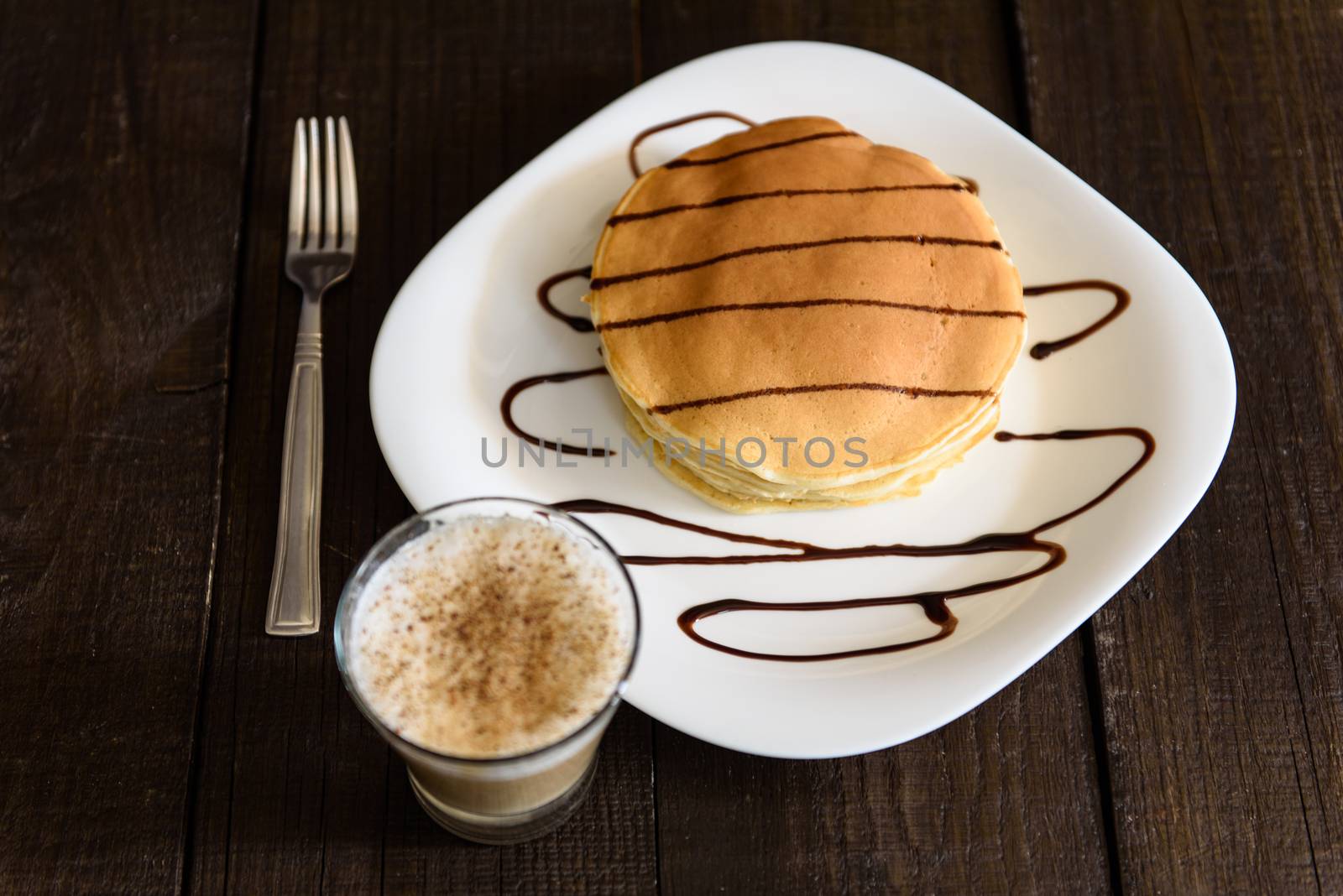 pancakes with chocolate topping and coffee cappuccino with corica on the table