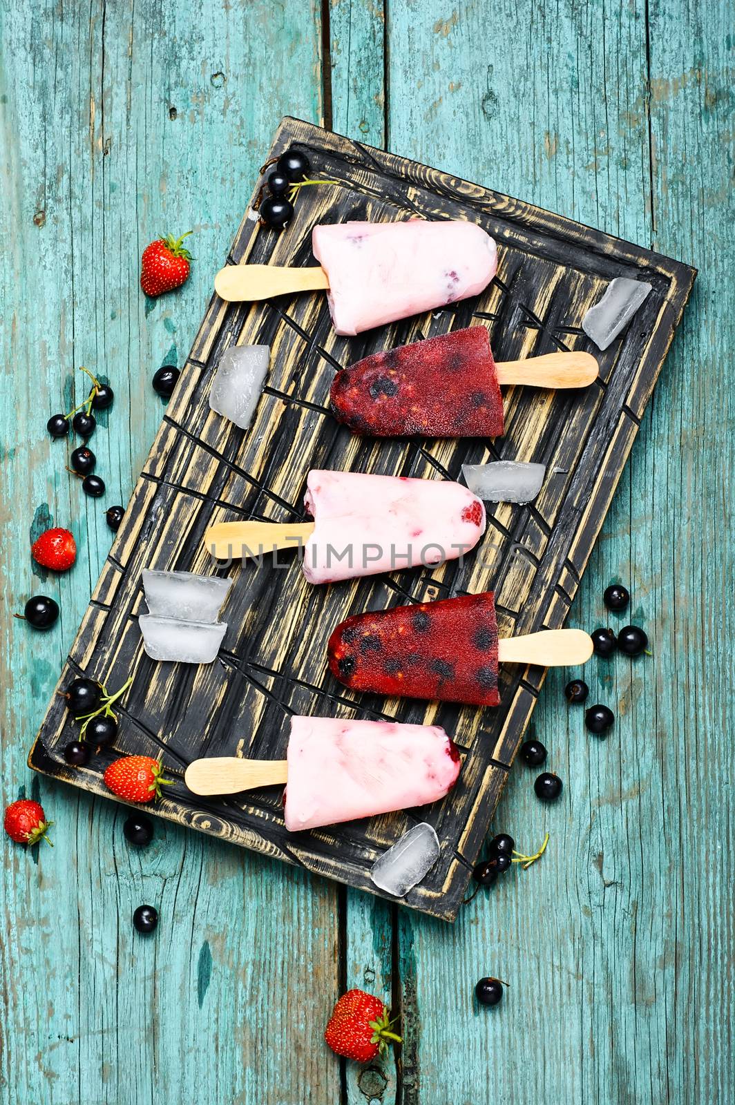 Berry ice cream on stick posted on stylish cutting board with berries and ice