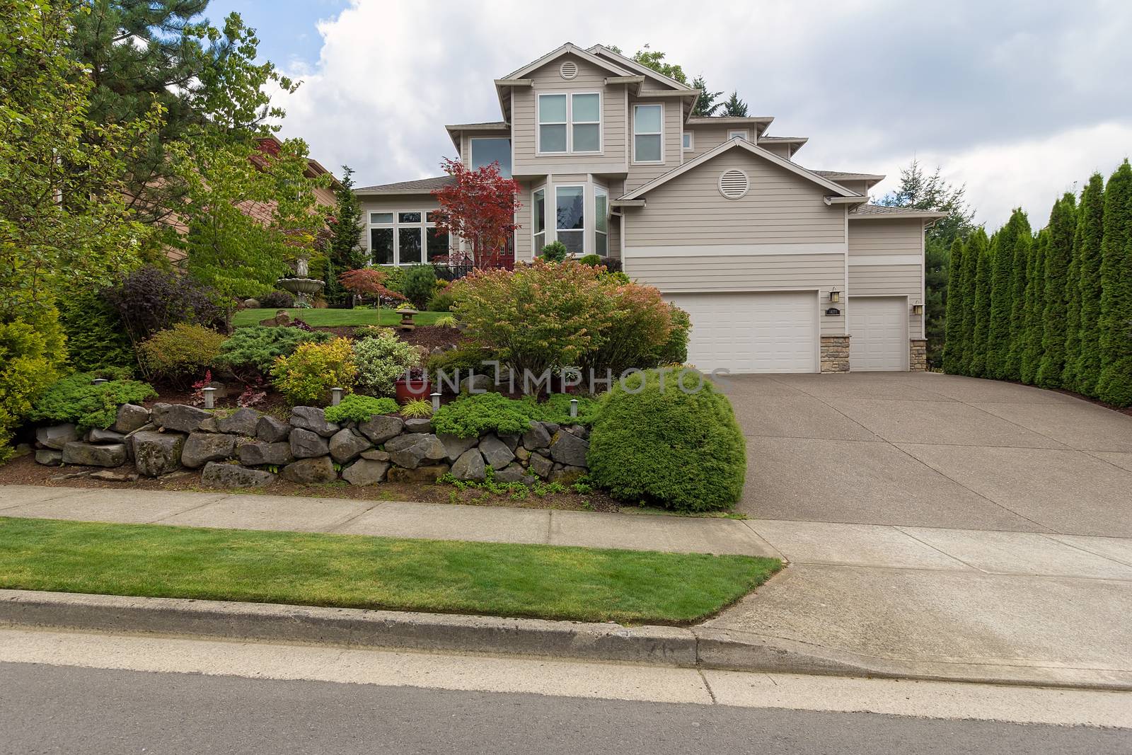 Traditional house with three car garage frontyard garden lush landscaping and green lawn in North America suburban neightborhood