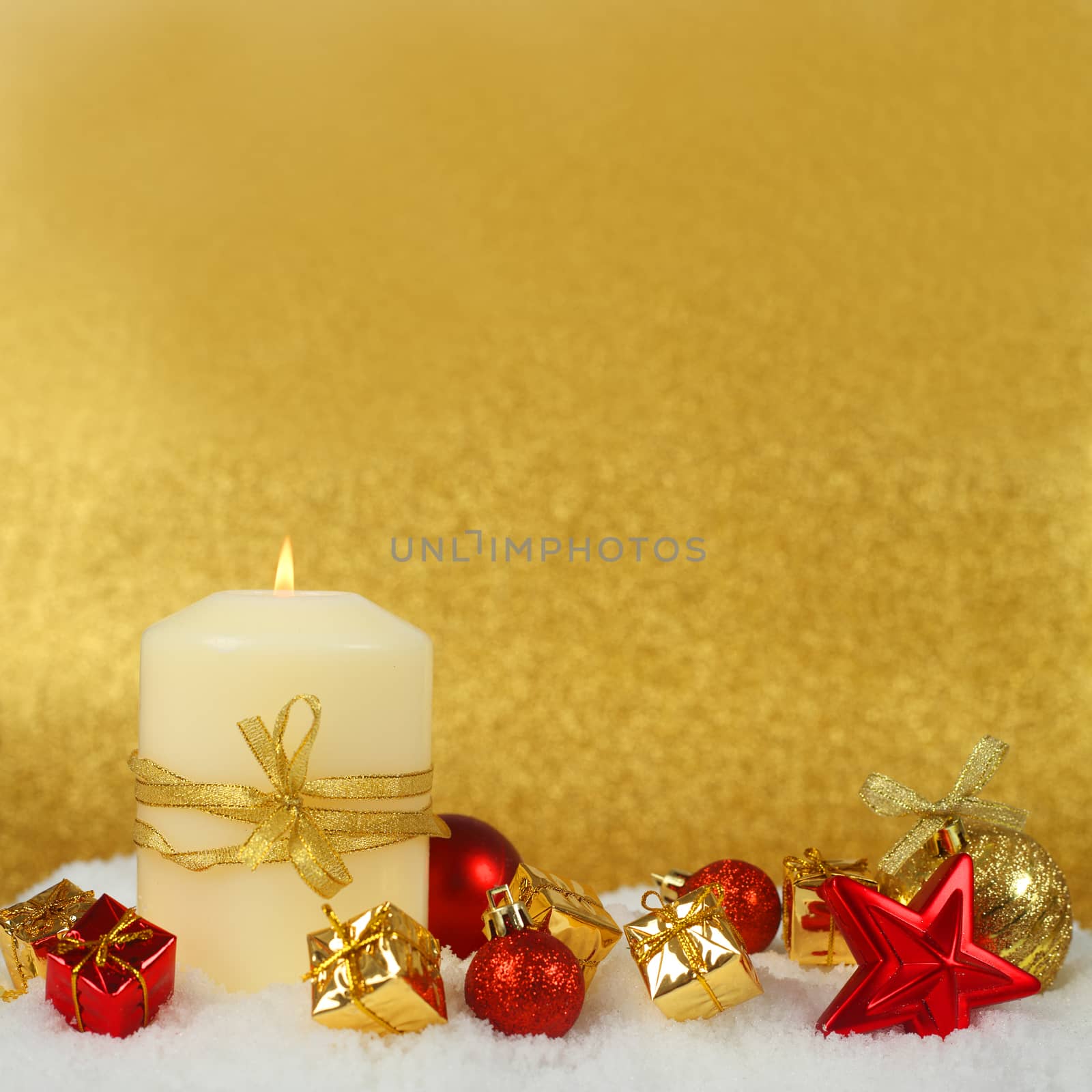Christmas decoration and burning candle on snow on golden background