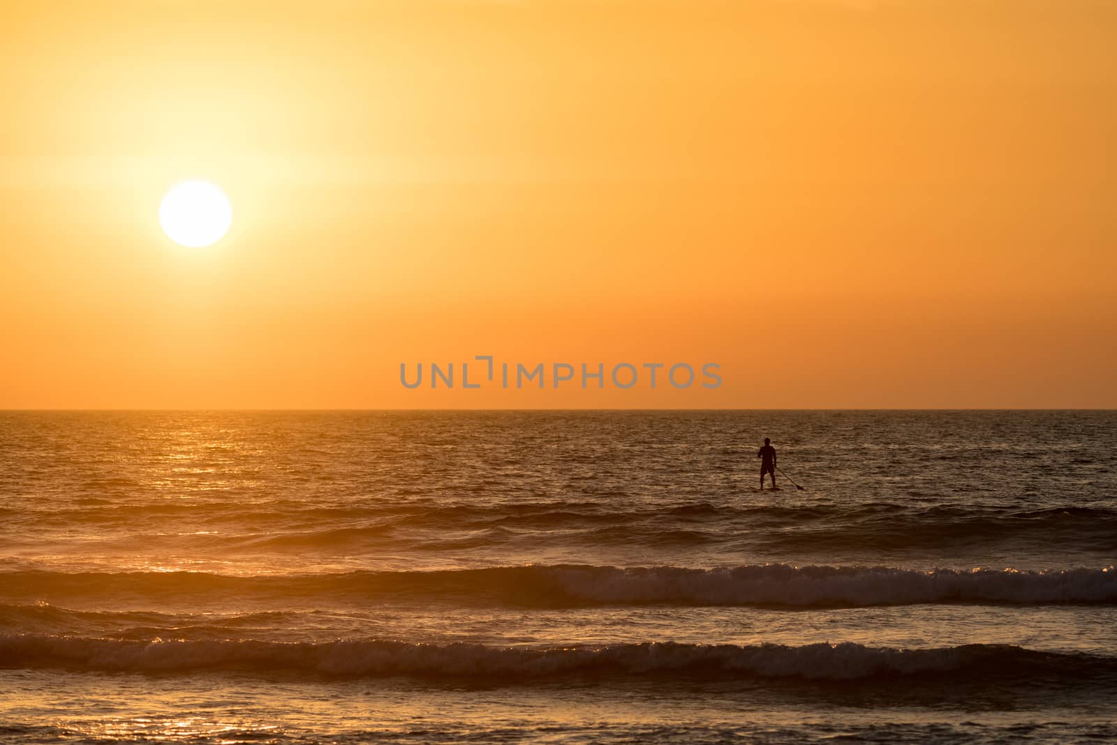 Man paddleboarding in open water at sunset