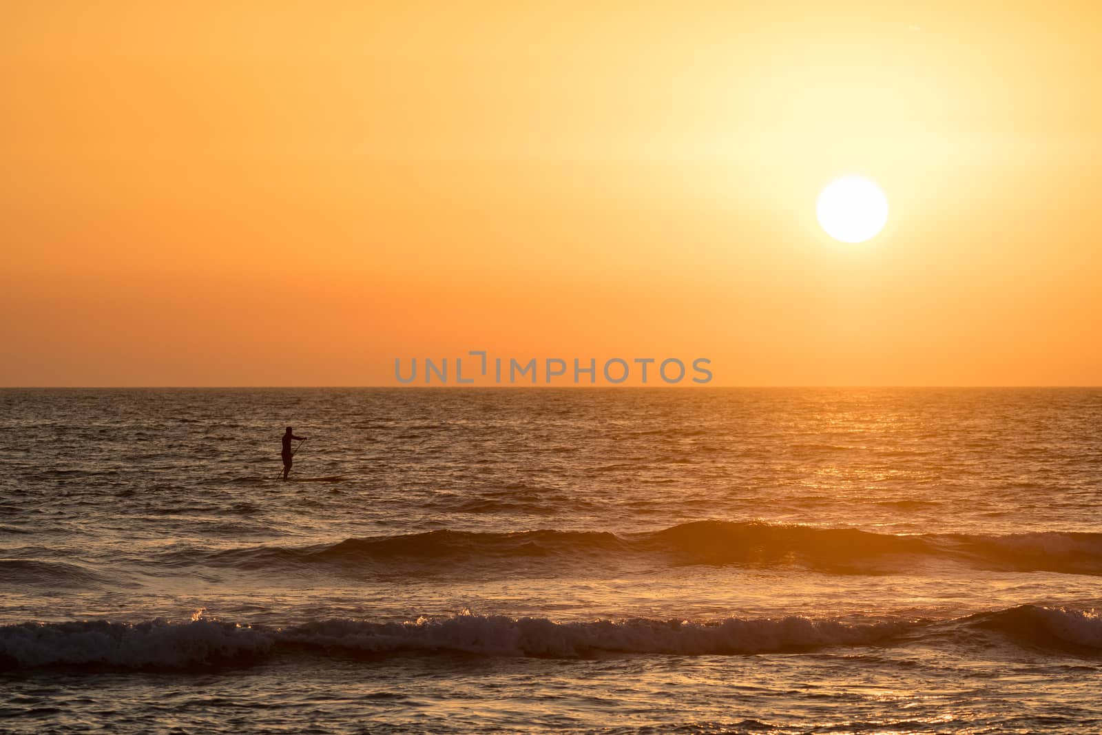 Man paddleboarding in open water at sunset