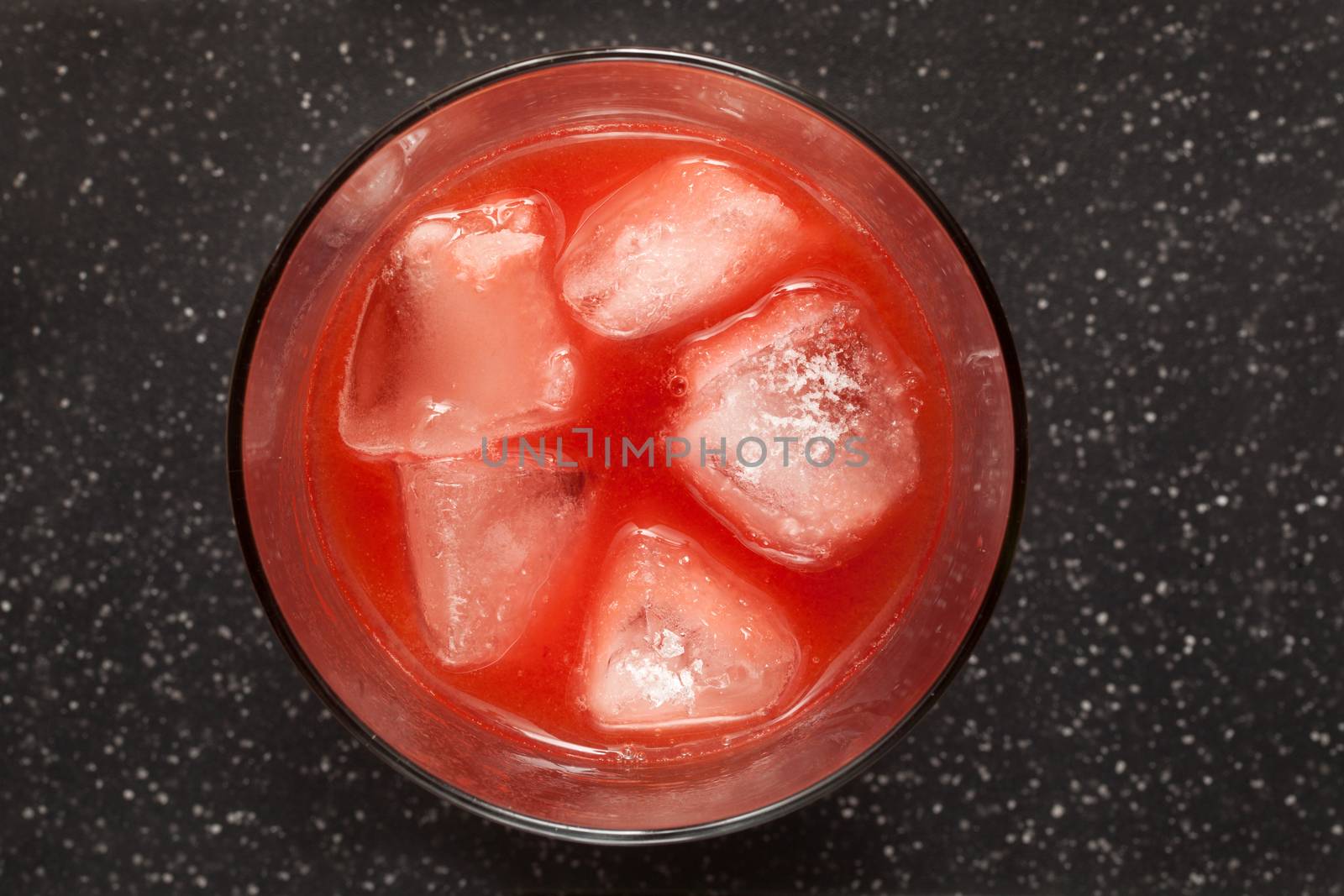Red juice of forest fruits with ice cubes on black table. Top view
