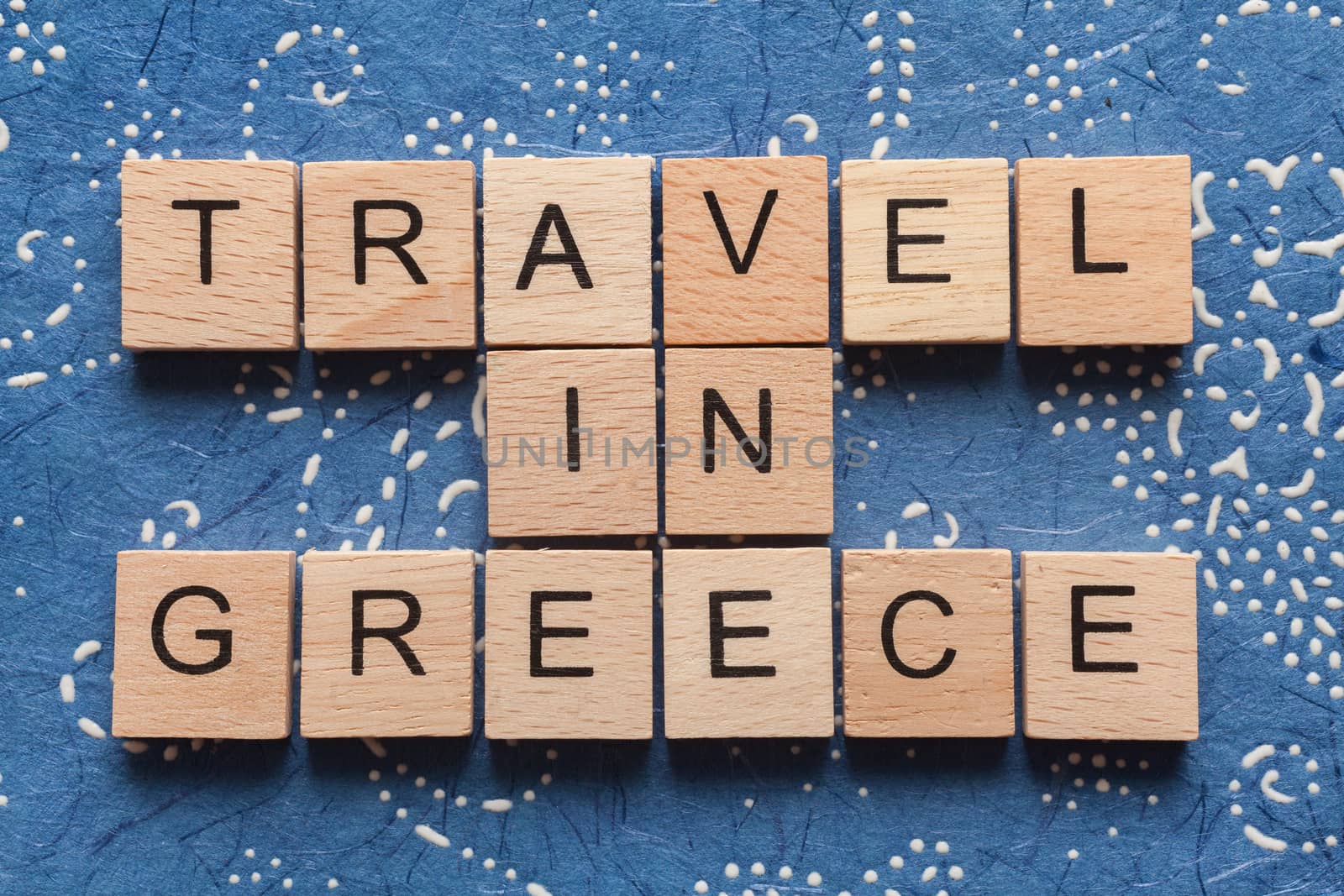 Wooden letters spelling TRAVEL IN GREECE on blue background