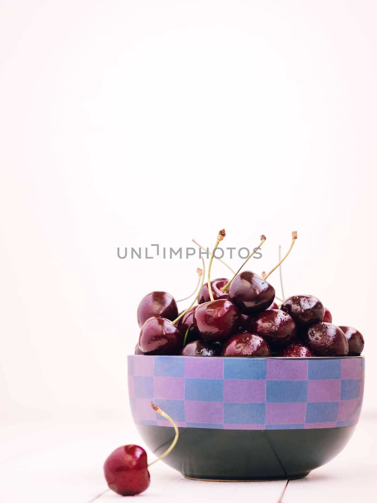 Heap of cherries in dish on white wooden table with copy space. Vertical orientation