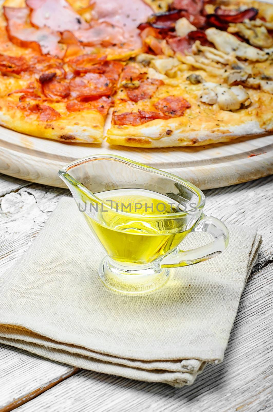 Gravy boat with olive oil on linen napkin to the pizza