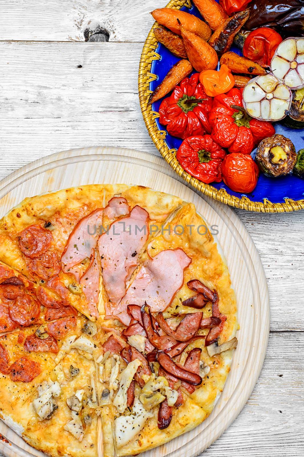 Pizza with meat and bacon and dish of roasted vegetables