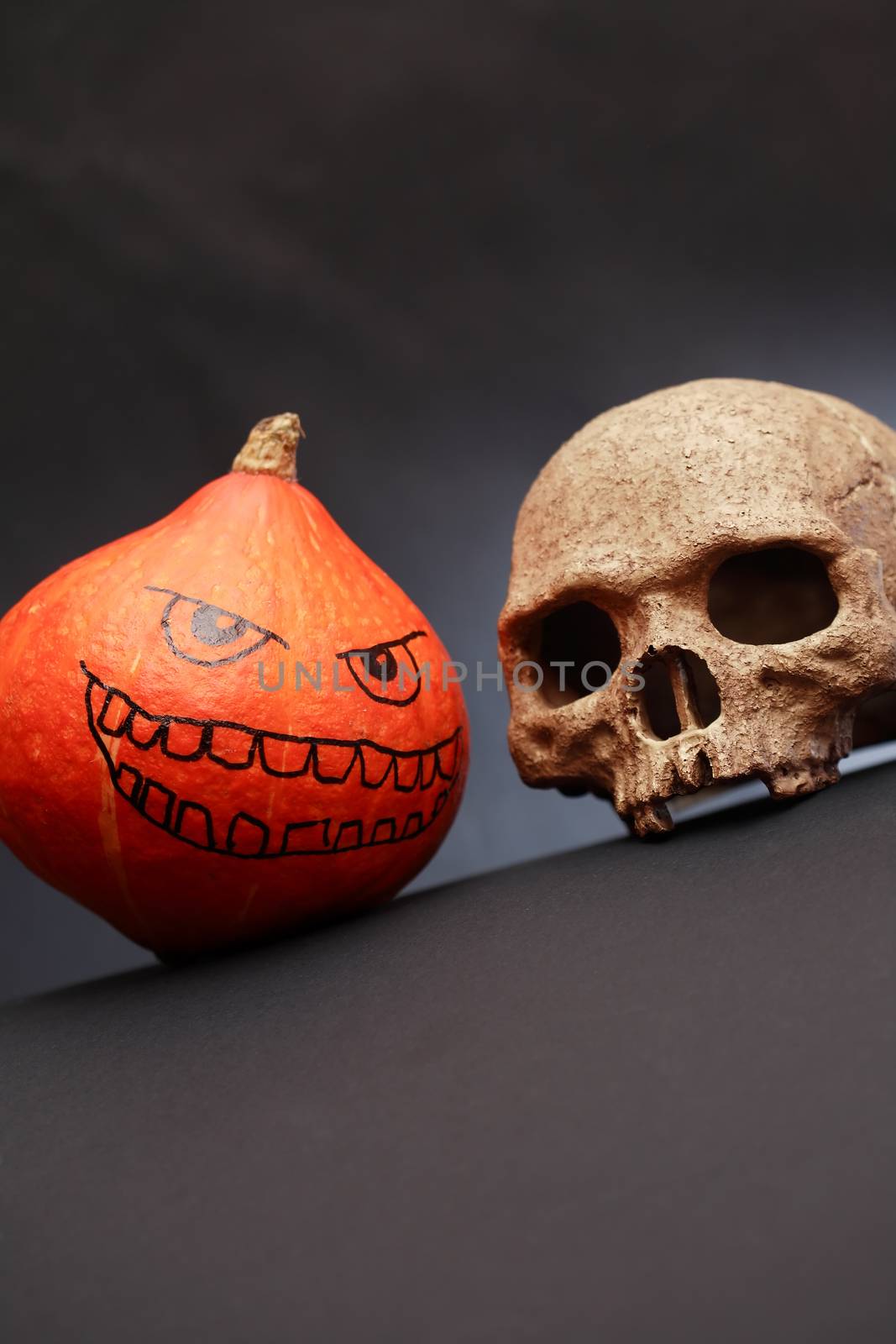 Halloween symbol. Pumpkin head near human skull on dark background