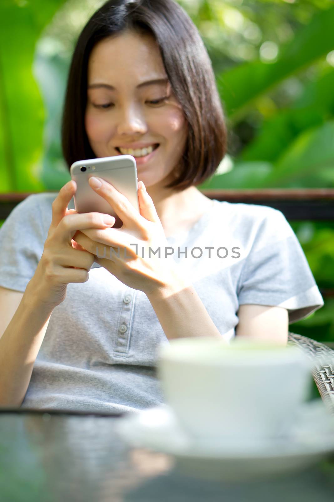 Woman Holding Mobile Phone In Front Of Coffee Cup by ekachailo