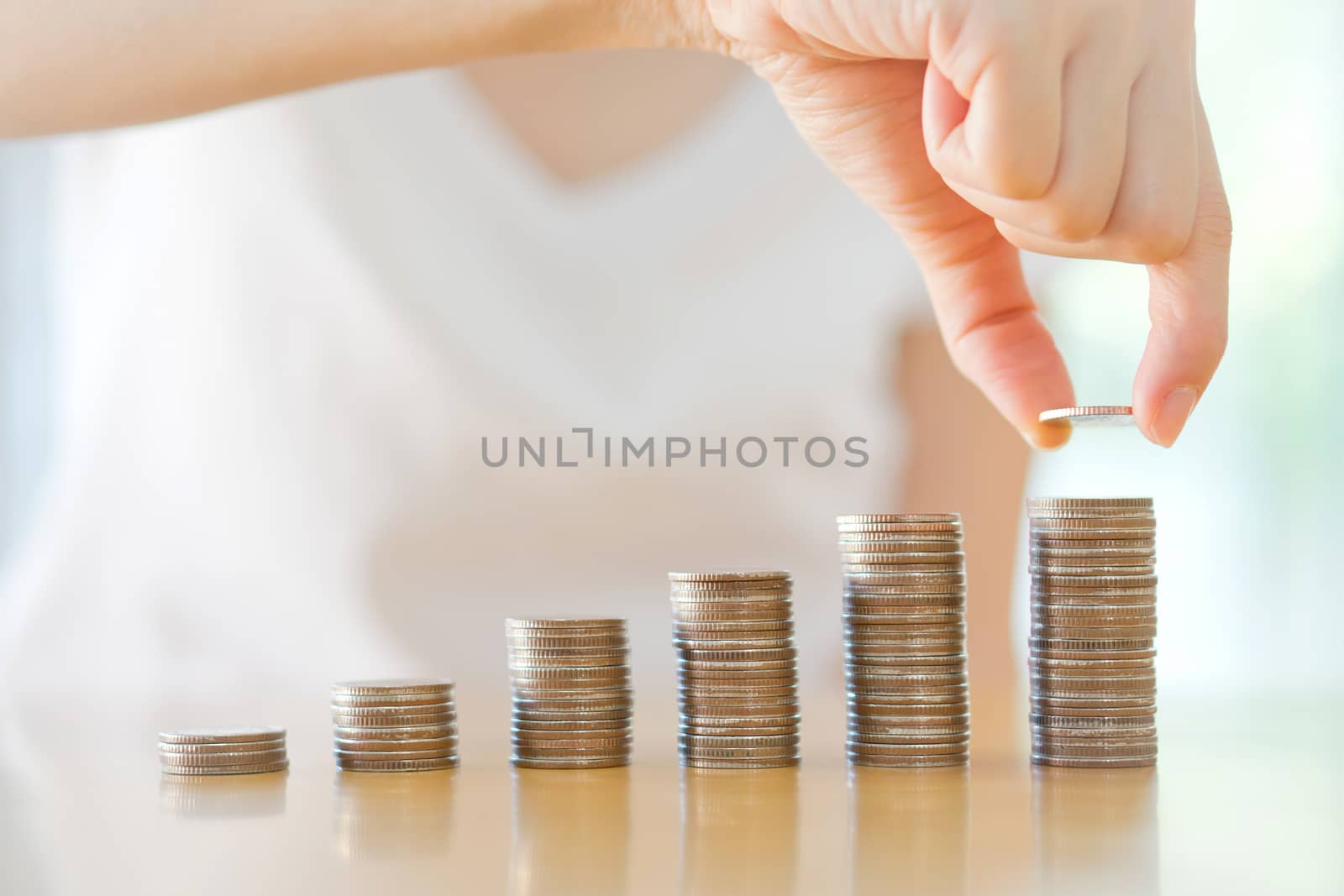 Close-up Of woman Putting Coin To Rising Stack Of Coins