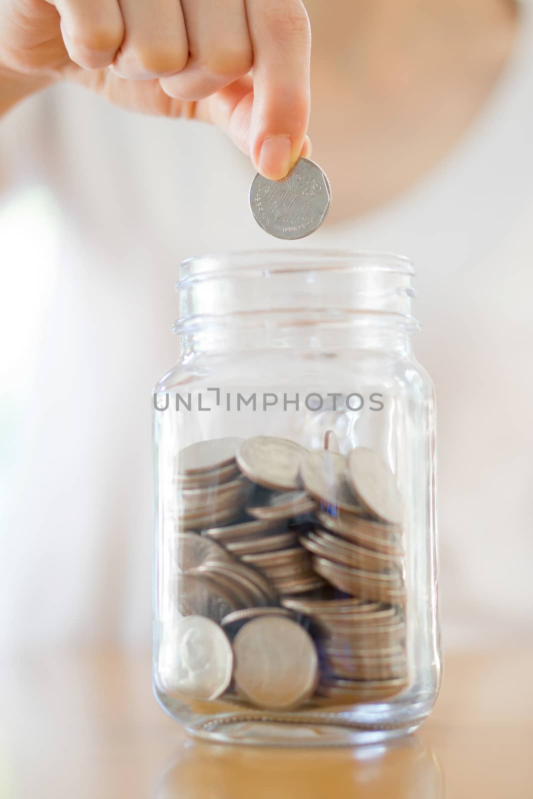 Woman Dropping Coins Into Glass Jar by ekachailo
