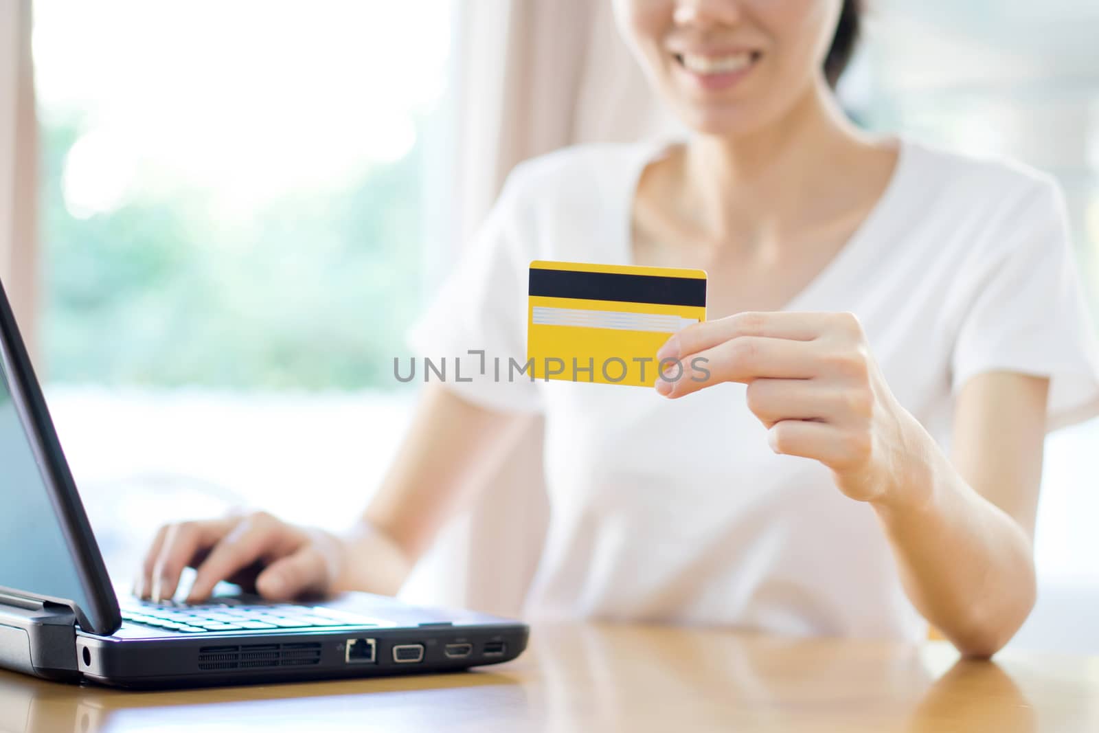 A woman smiling and looking in front of her as she uses her credit card with her laptop.
