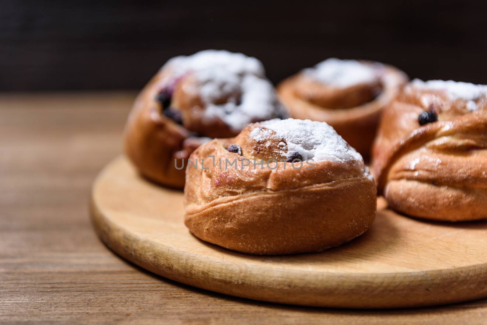 bun with currants covered with powdered sugar lay on a chopping board brown