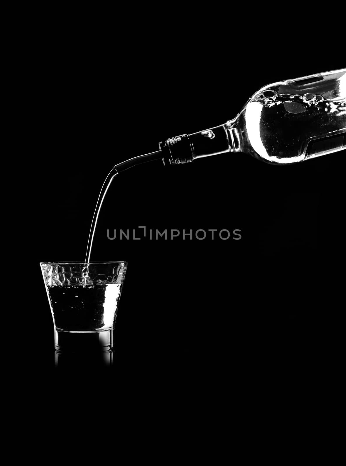 in a glass on the table poured white wine from the bottle through the dispenser on black background