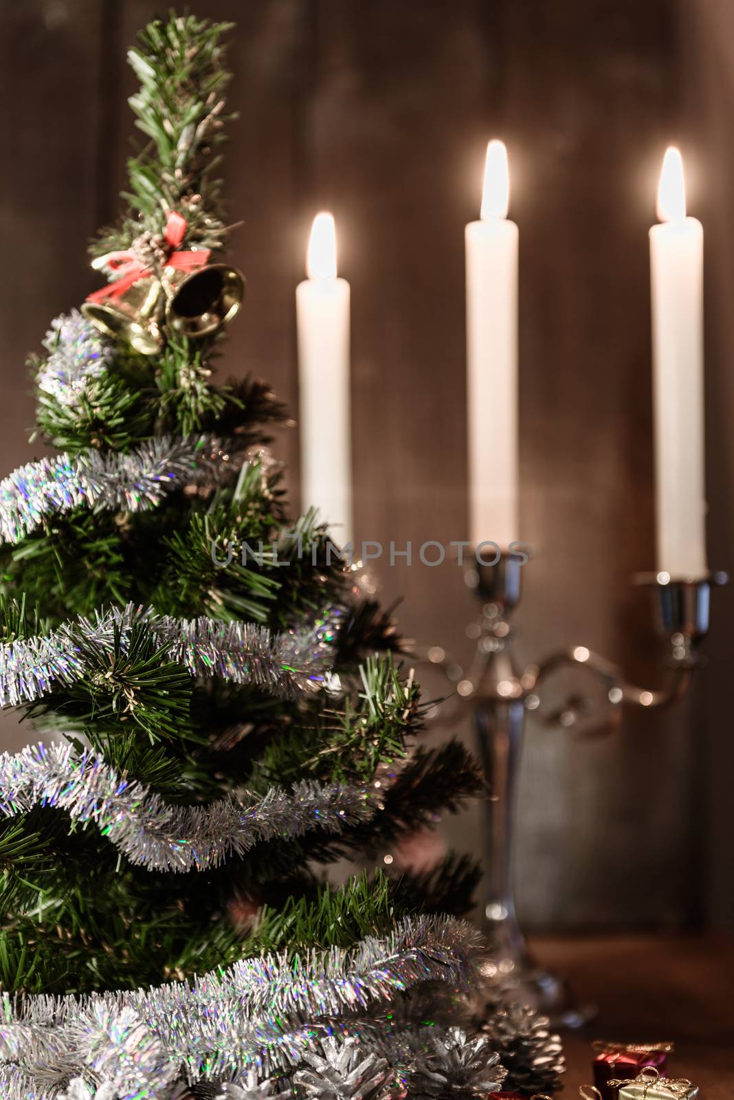 Christmas decorative tree is adorned with rain stands on the table with lit candles