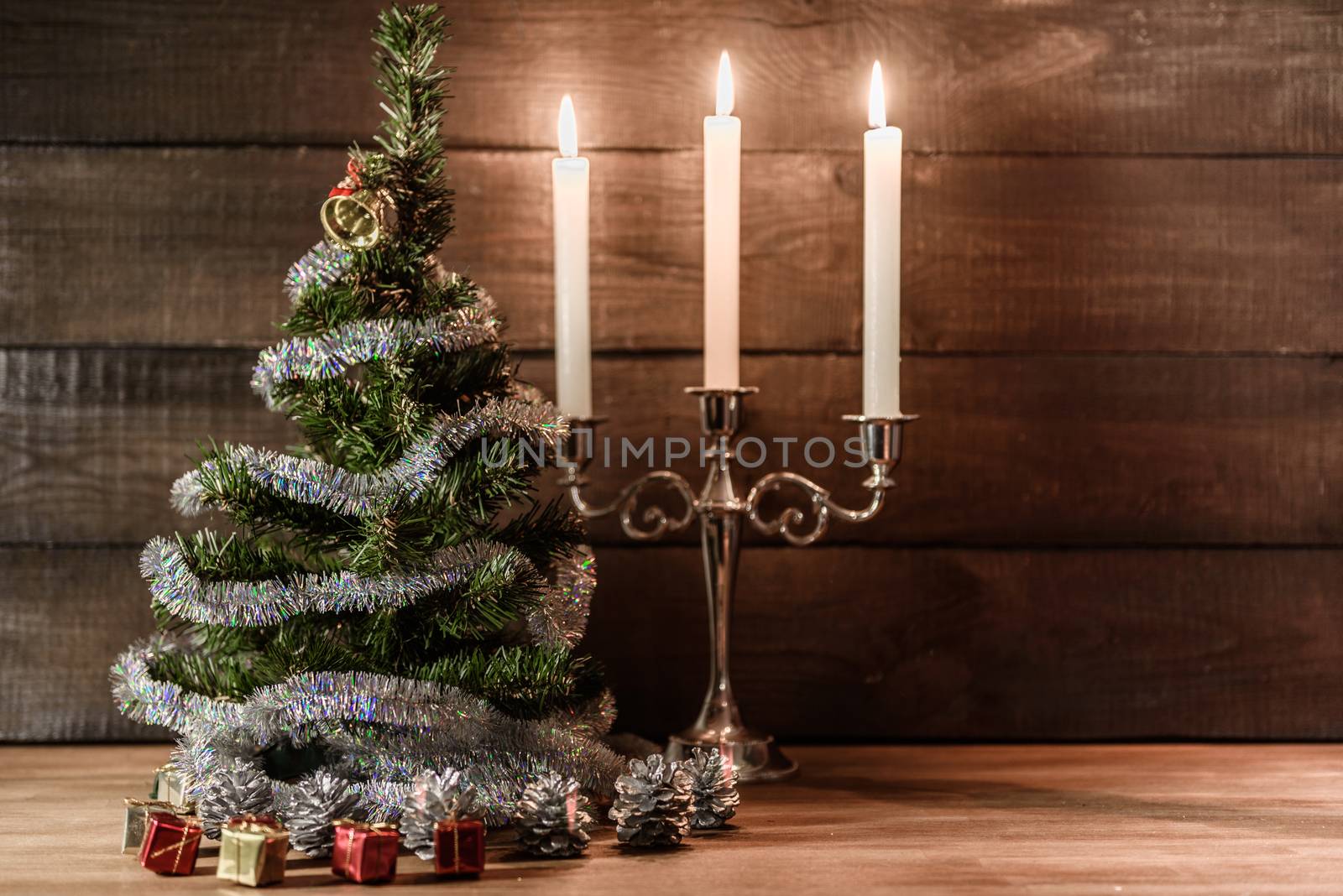 Christmas decorative tree is adorned with rain stands on the table with lit candles