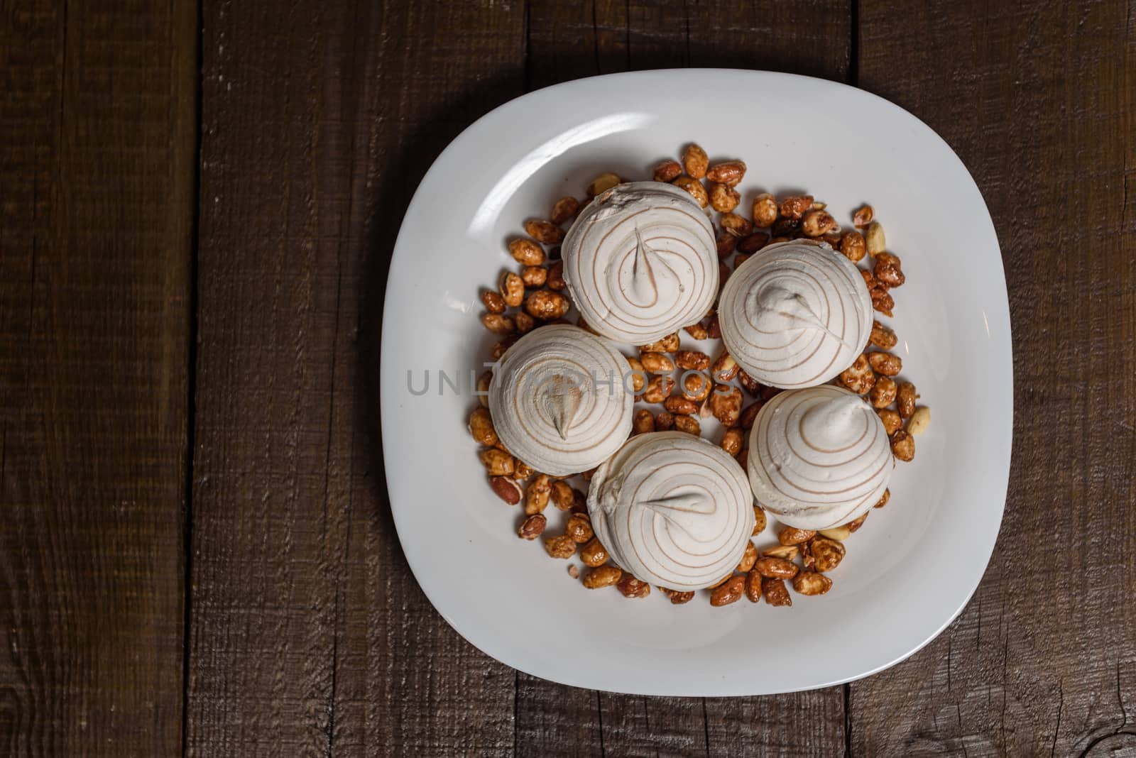 white marshmallows and sweet peanuts on the plate and wood