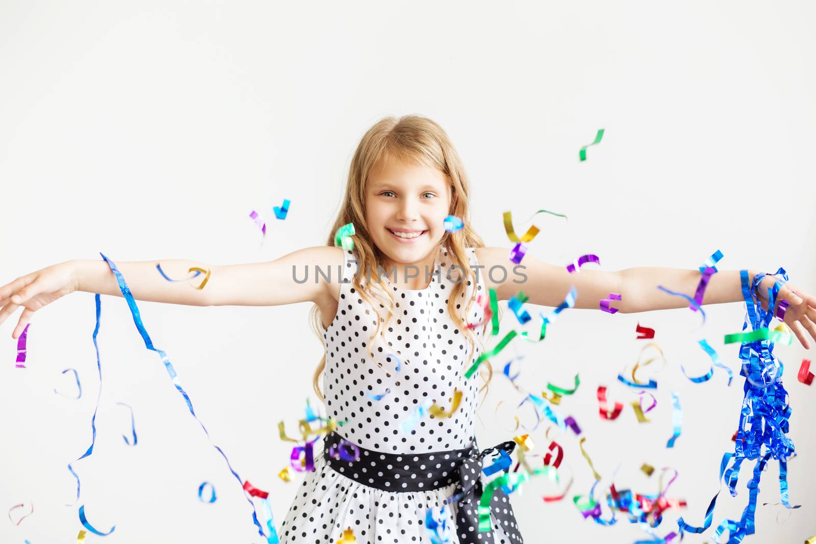 Little girl jumping and having fun celebrating birthday. Portrait of a child throws up multi-colored tinsel and confetti. Positive emotions. Happy excited laughing kid under sparkling confetti shower