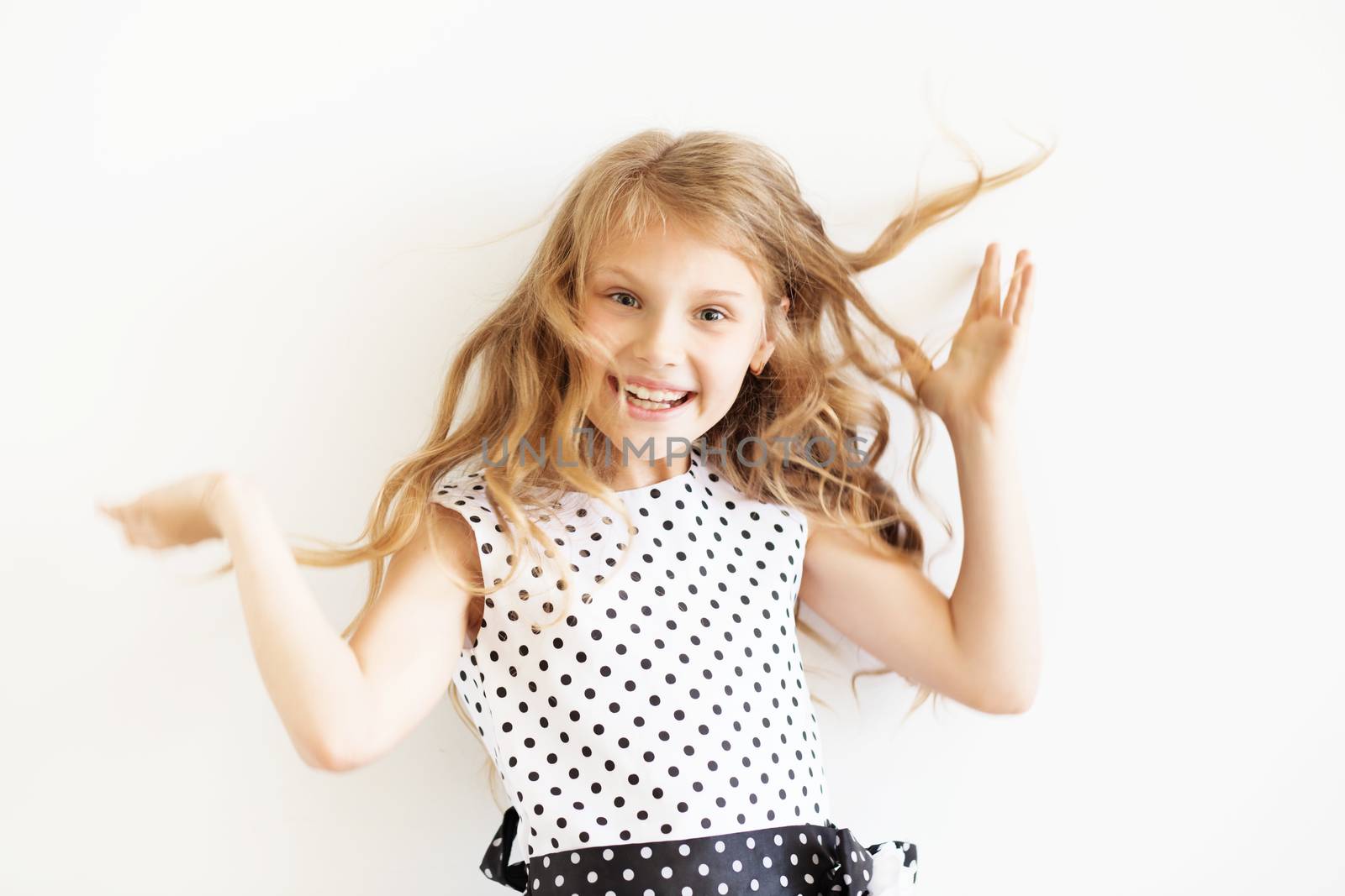 Lovely frisky little girl in a polka-dot dress jumping and having fun against a white background. Happy kids