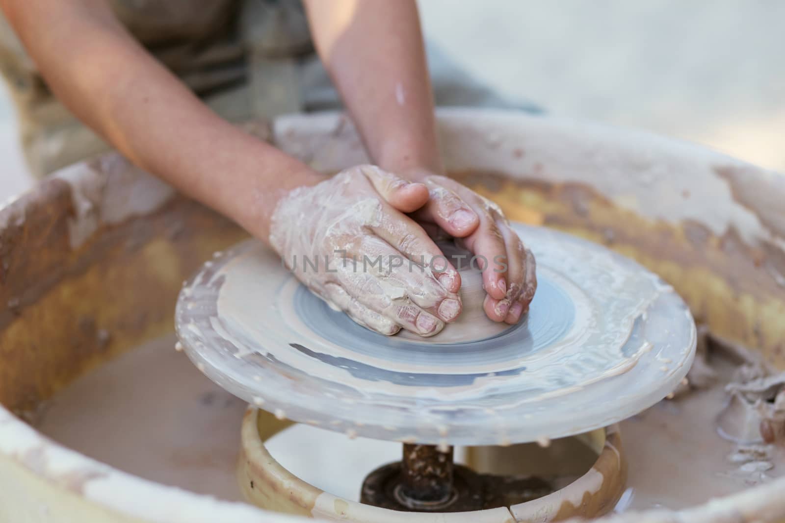 Hands of young potter, creating an earthen jar on the circle, close-up