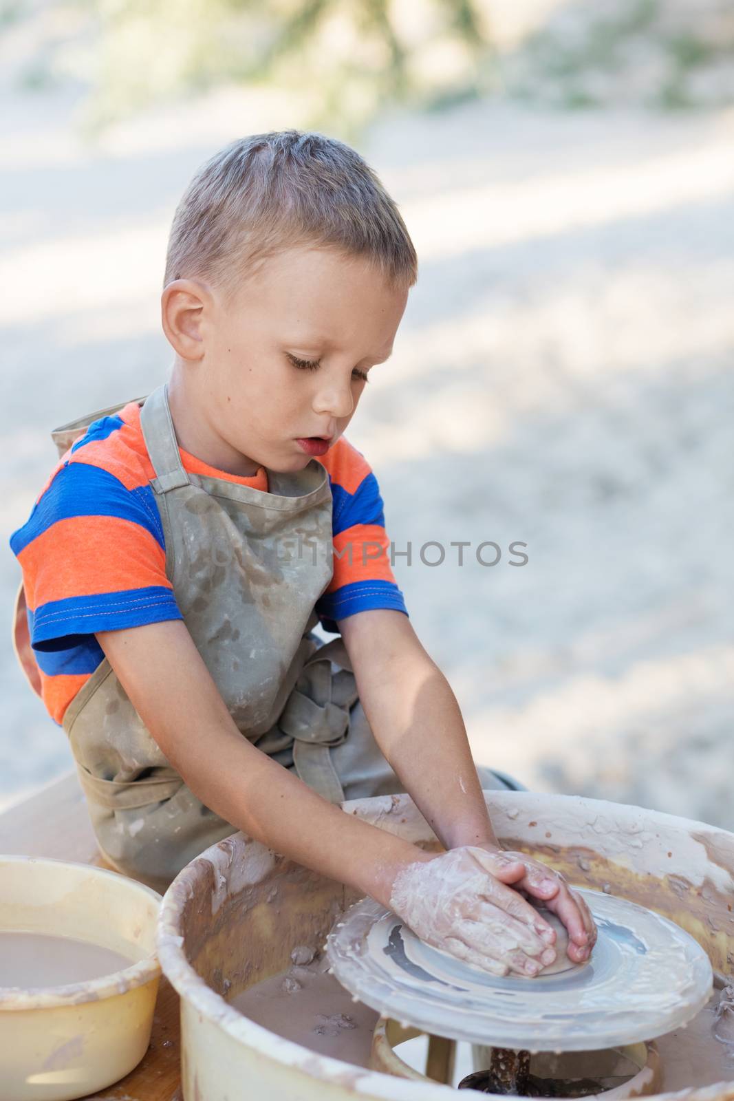 Little smiling boy produced on potters wheel pot. Hands of young potter, was produced on range of pot. The hands of a potter, creating an earthen jar on the circle, close-ups