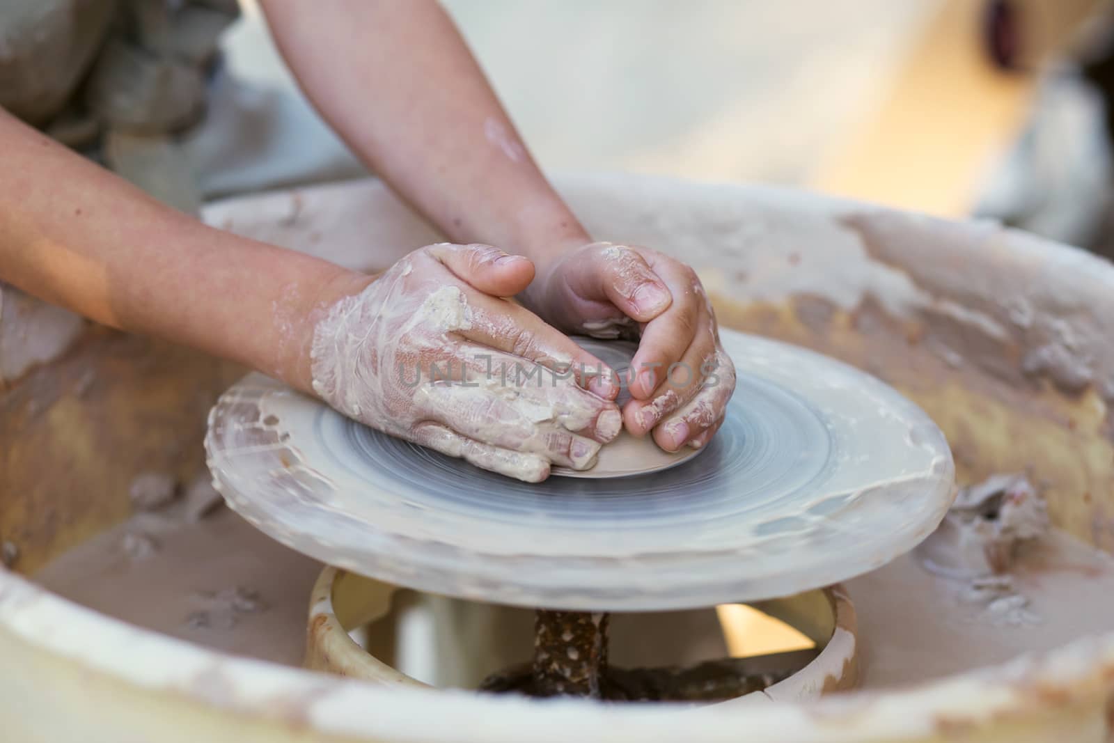 Hands of young potter, creating an earthen jar on the circle, close-up