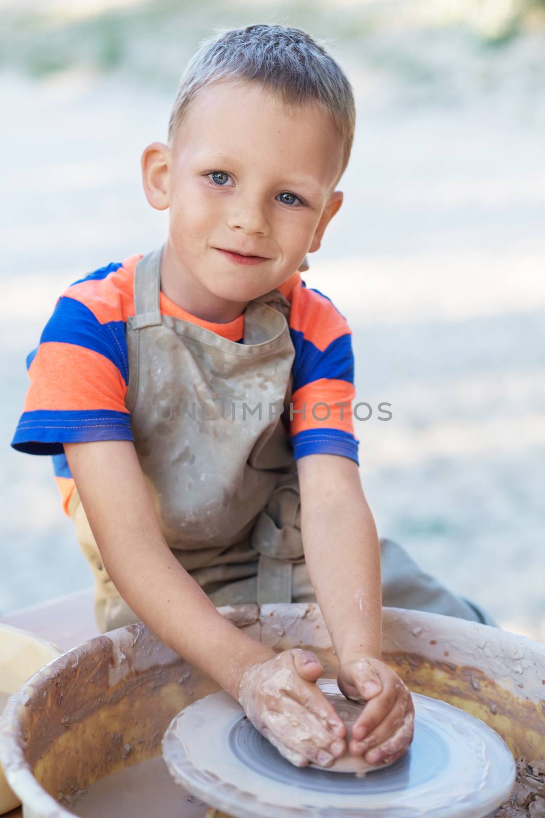 Little smiling boy produced on potters wheel pot. Hands of young potter, creating an earthen jar on the circle, close-up